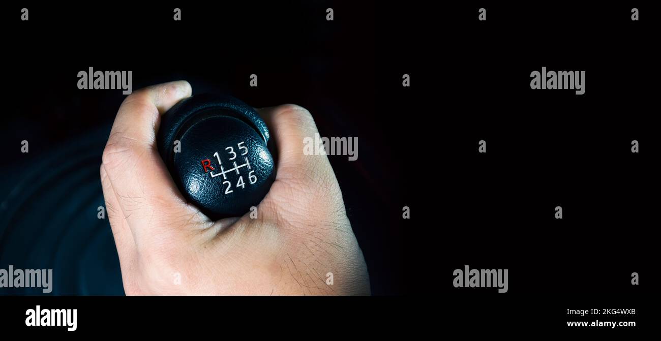 The driver hand is shifting the gears of a 6-speed manual transmission, panoramic banner with copy space on black background Stock Photo