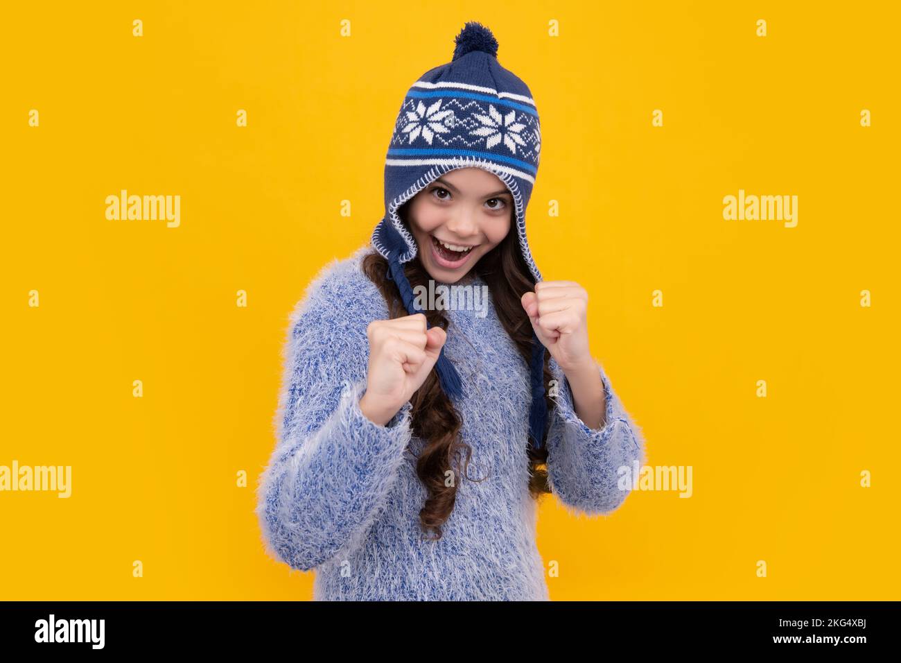 Beautiful winter kids portrait. Teenager girl posing with winter sweater and knit hat on yellow background. Excited teenager girl. Stock Photo