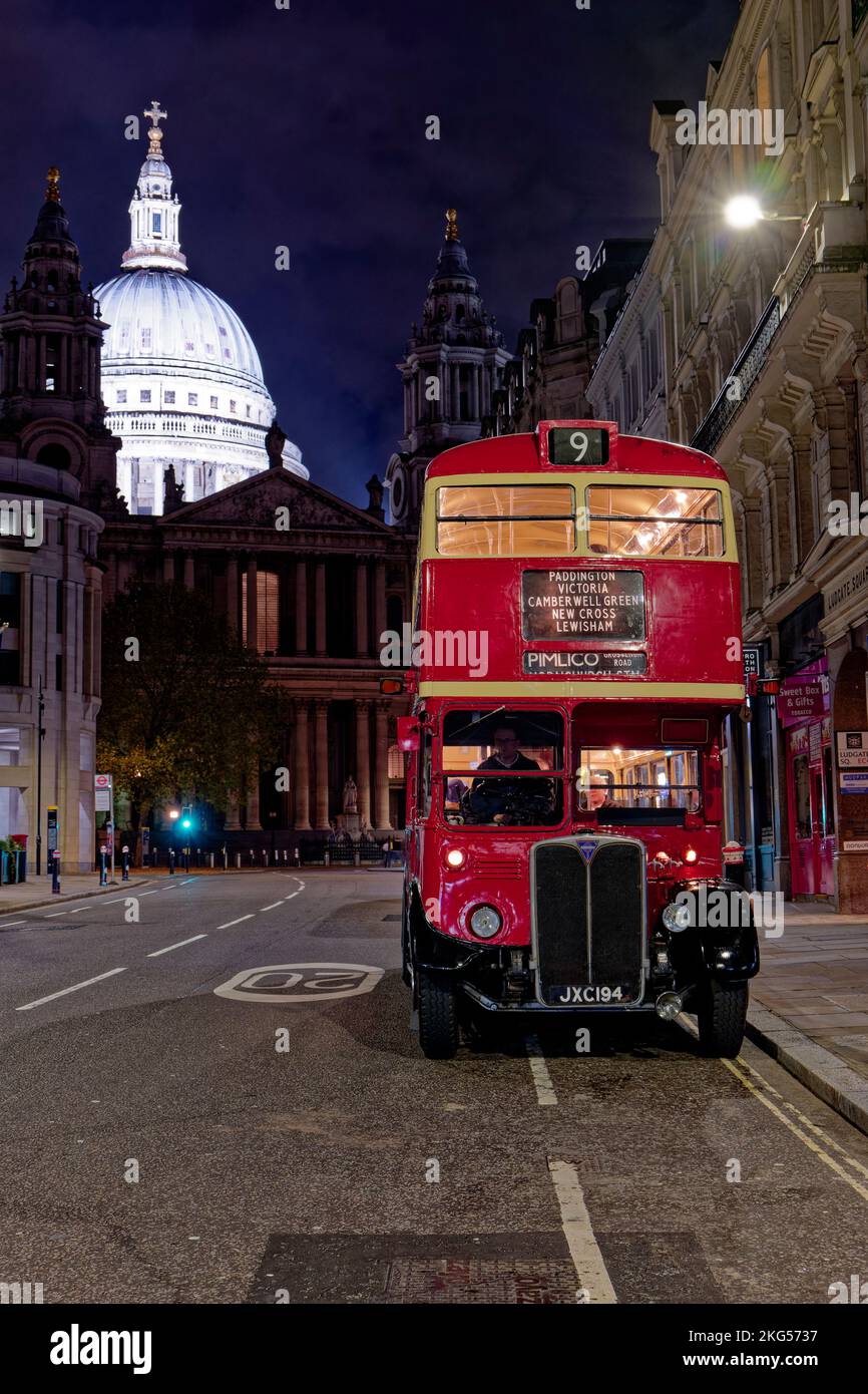 Classic old double decker London bus parked at night along Ludgate Hill in London with the illuminated white dome of St Paul's Cathedral behind Stock Photo