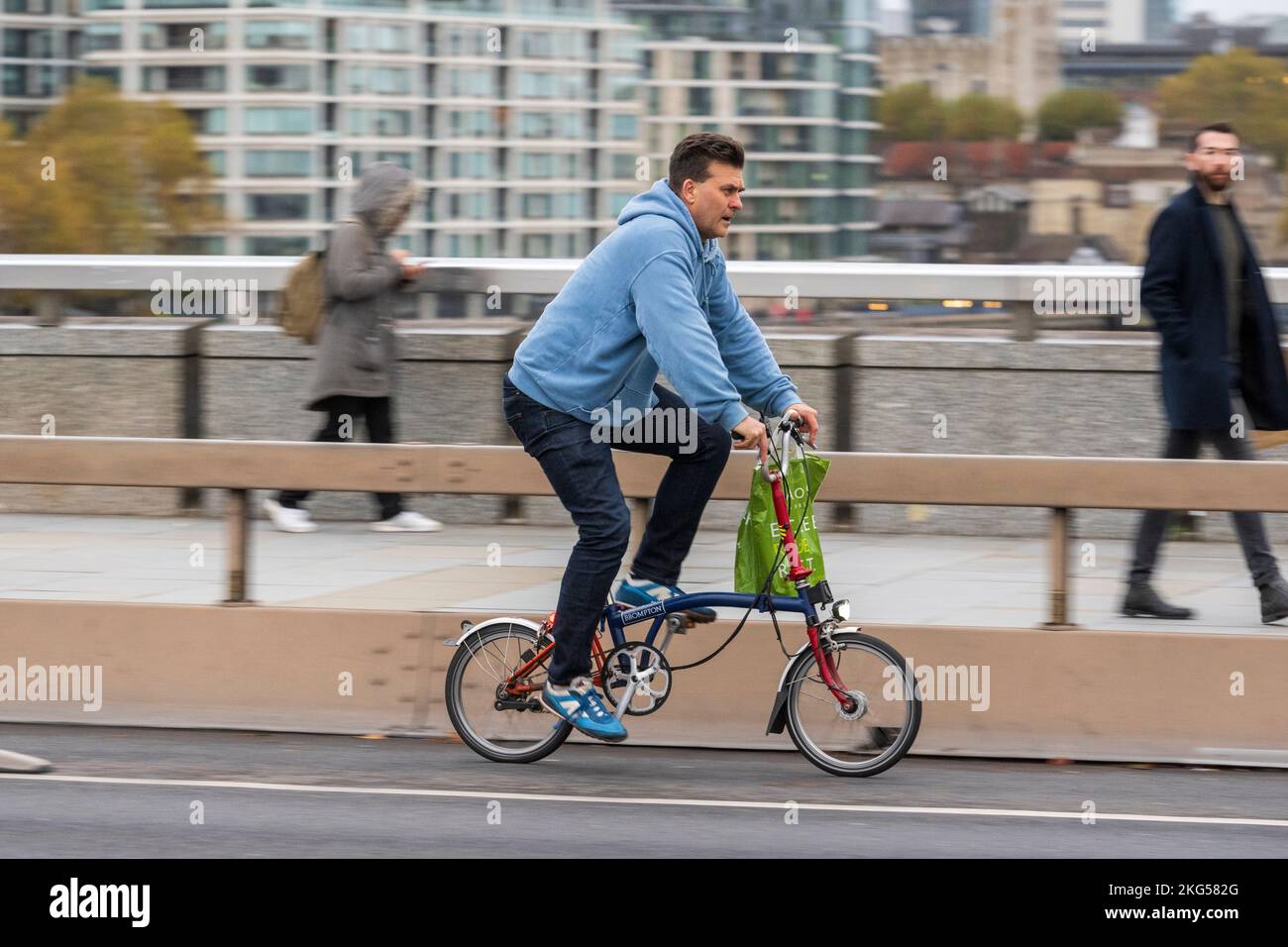 A man commuting, during the rush hour on a Brompton folding bicycle across London Bridge, London, UK.  16 Nov 2022 Stock Photo