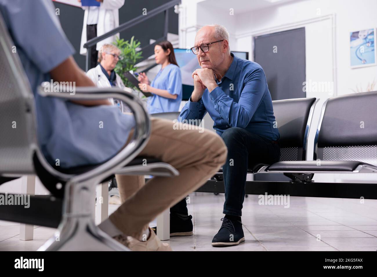 Stressed exhausted senior man patient sitting on chair in hospital reception waiting for physician medic to discuss disease diagnosis during checkup visit consultation. Health care service and concept Stock Photo