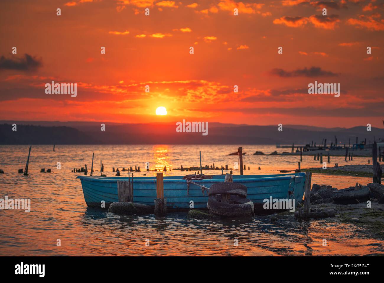 Sunset over lake, wooden pier and old fishing boat Stock Photo