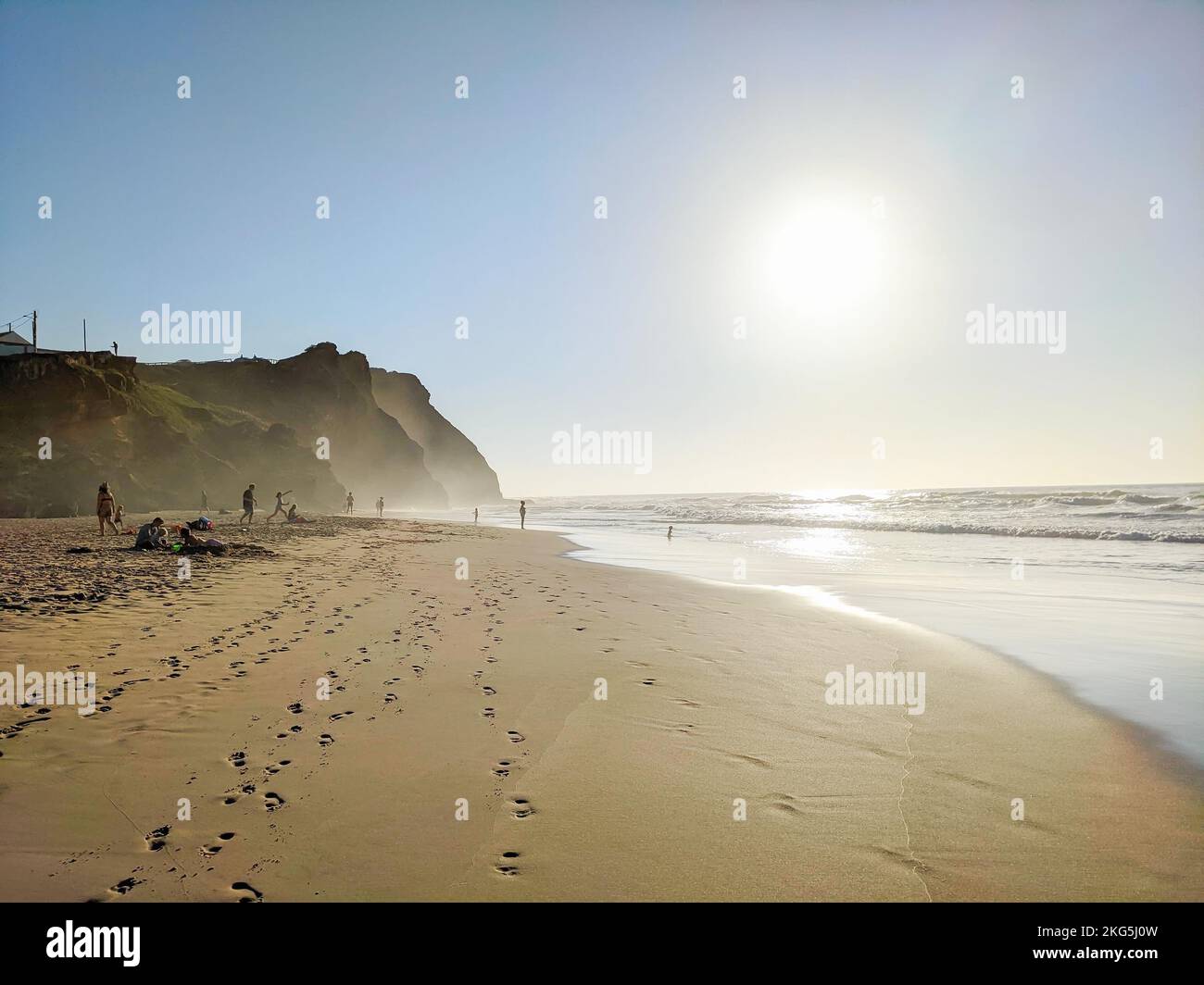 Beach Monte Clairgo cliffs in evening sunshine haze, people relaxing on sand, footprints, Atlantic ocean coast, Aljezur, Portugal Stock Photo