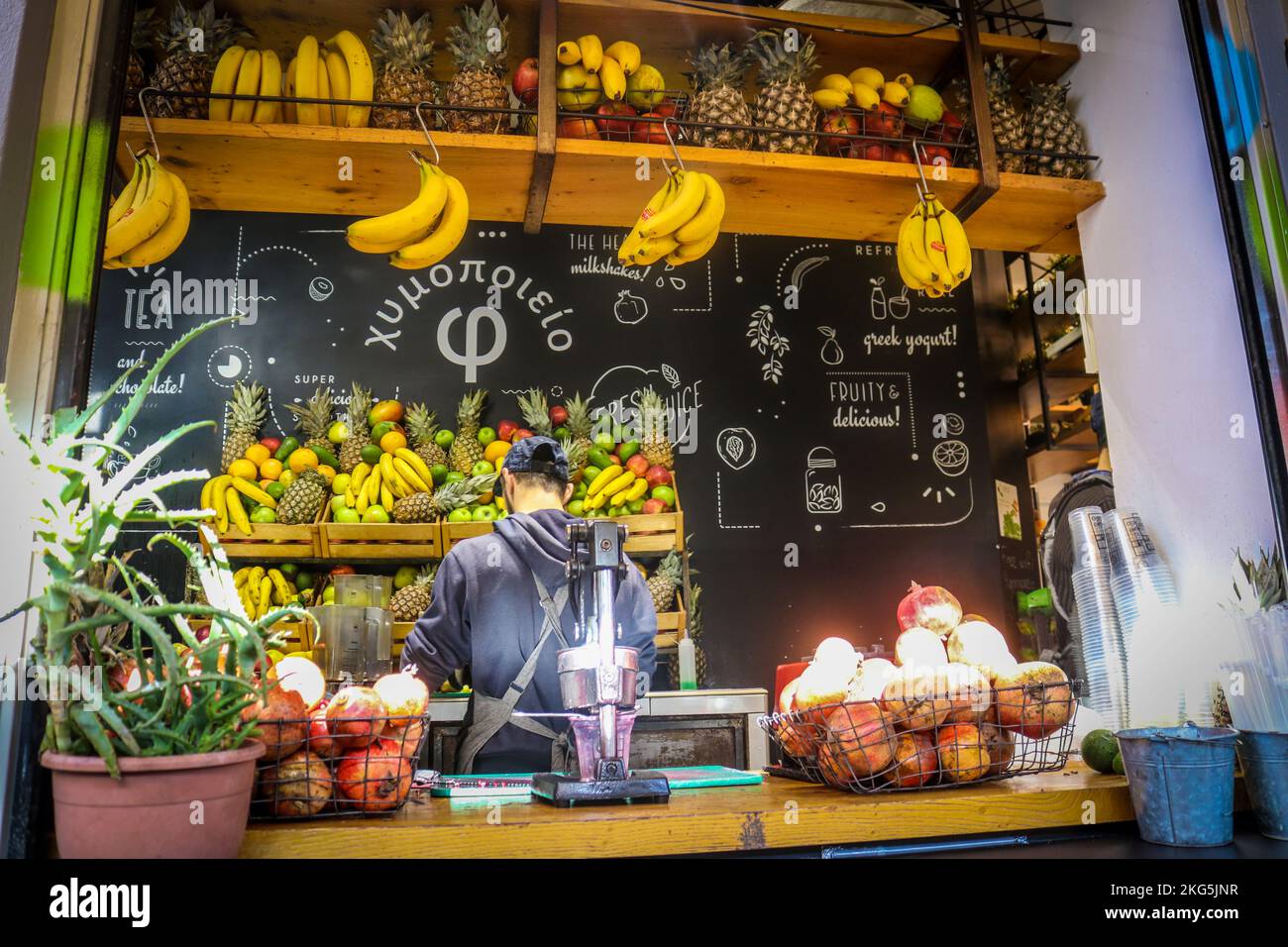 01-03-2018 Athens Greece - Open air fFruit juice stand with male server and piles of fruit - Bright sun shining in Stock Photo
