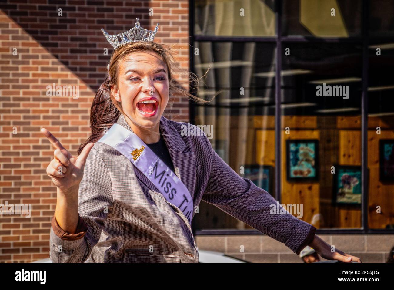 10-22-2022 Tulsa USA - Beautiful girl who has won Miss Tulsa contest rides convertible in Halloween Parade with big smile as she gives Go Pokes  sign Stock Photo