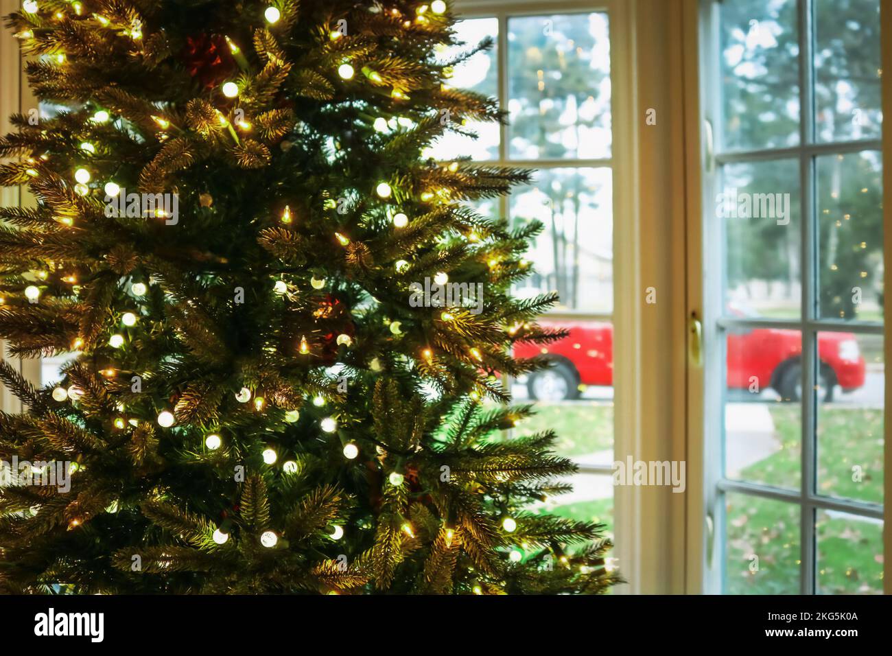 Christmas in the South - Christmas tree with lights in front of a blurred bay window showing green grass and trees and a red pickup truck Stock Photo