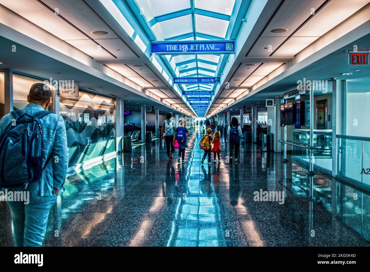 Jume 20 2022 Tulsa OK USA - Airport corridor with skylight and signs saying Time is a JetPlane - Man in backpack passing Military Lounge - A family wa Stock Photo