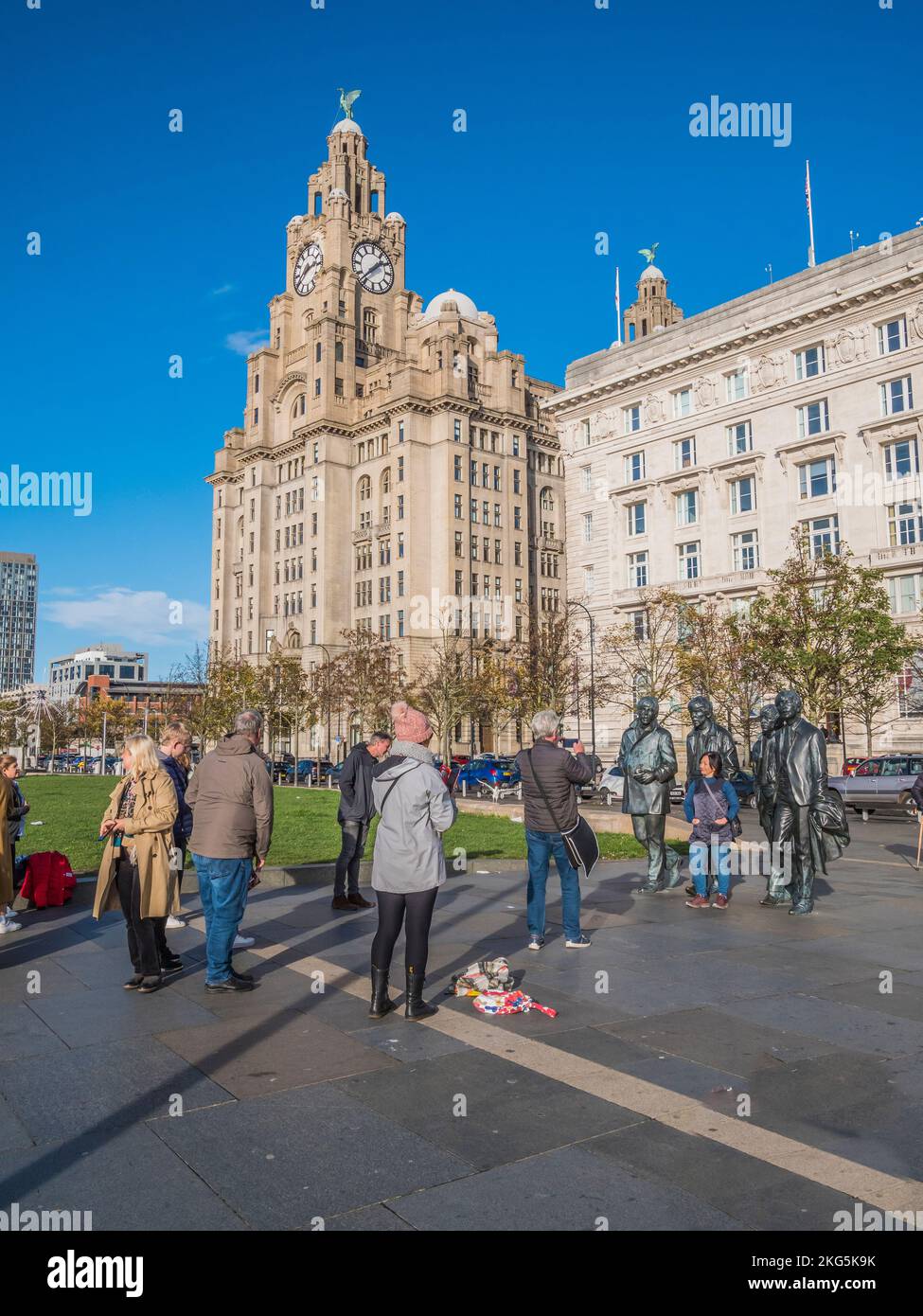 Street scene in Liverpool with tourists queueing to have selfies with the statues of the famous Beatles pop group, along with the Liver Building Stock Photo
