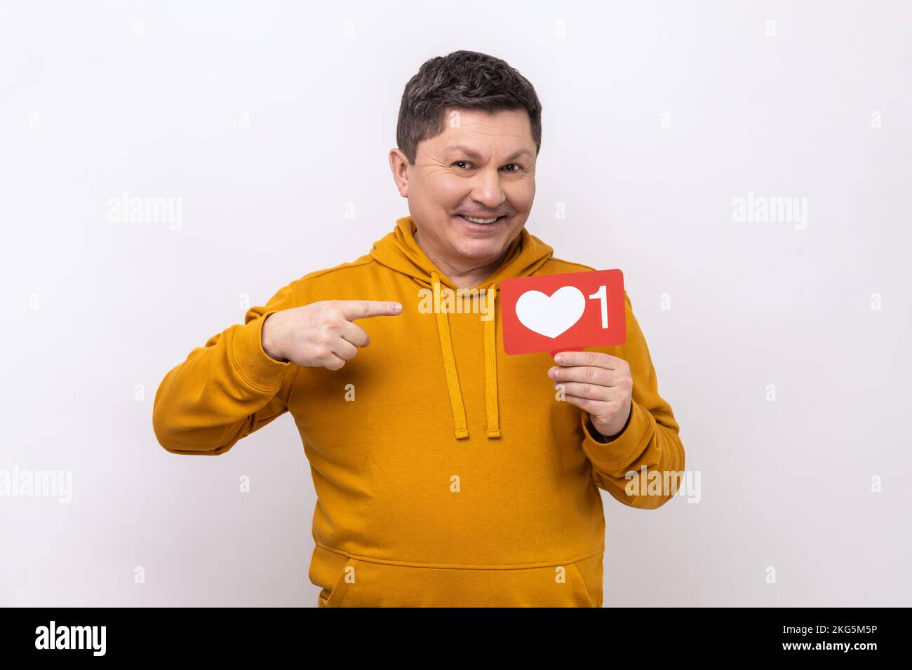 Internet blogging. Portrait of joyful man pointing at heart like icon, recommending to click on social media button, wearing urban style hoodie. Indoor studio shot isolated on white background. Stock Photo