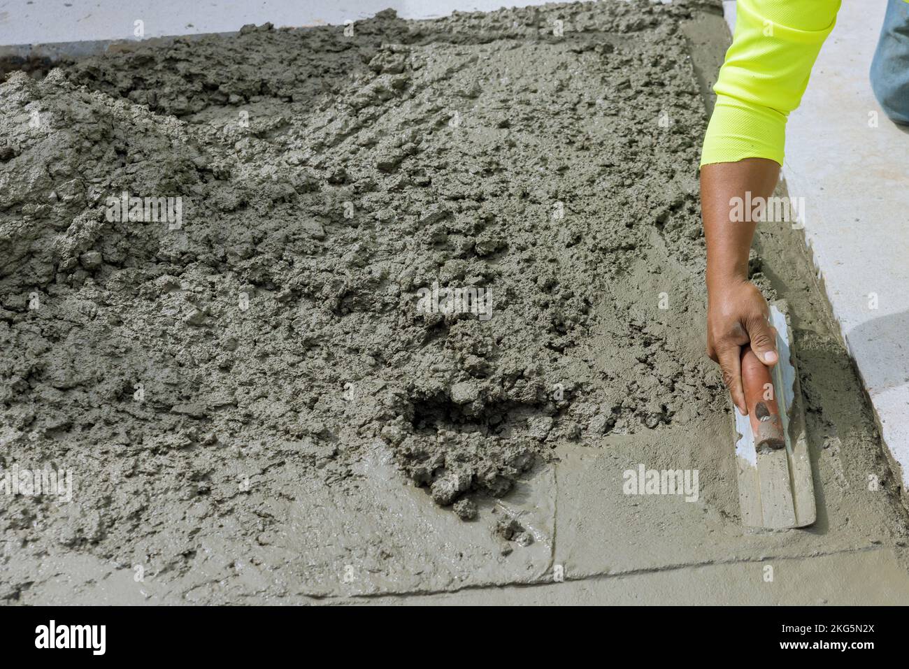 On freshly poured concrete sidewalk worker holds steel trowel in process of smoothing it leveling Stock Photo
