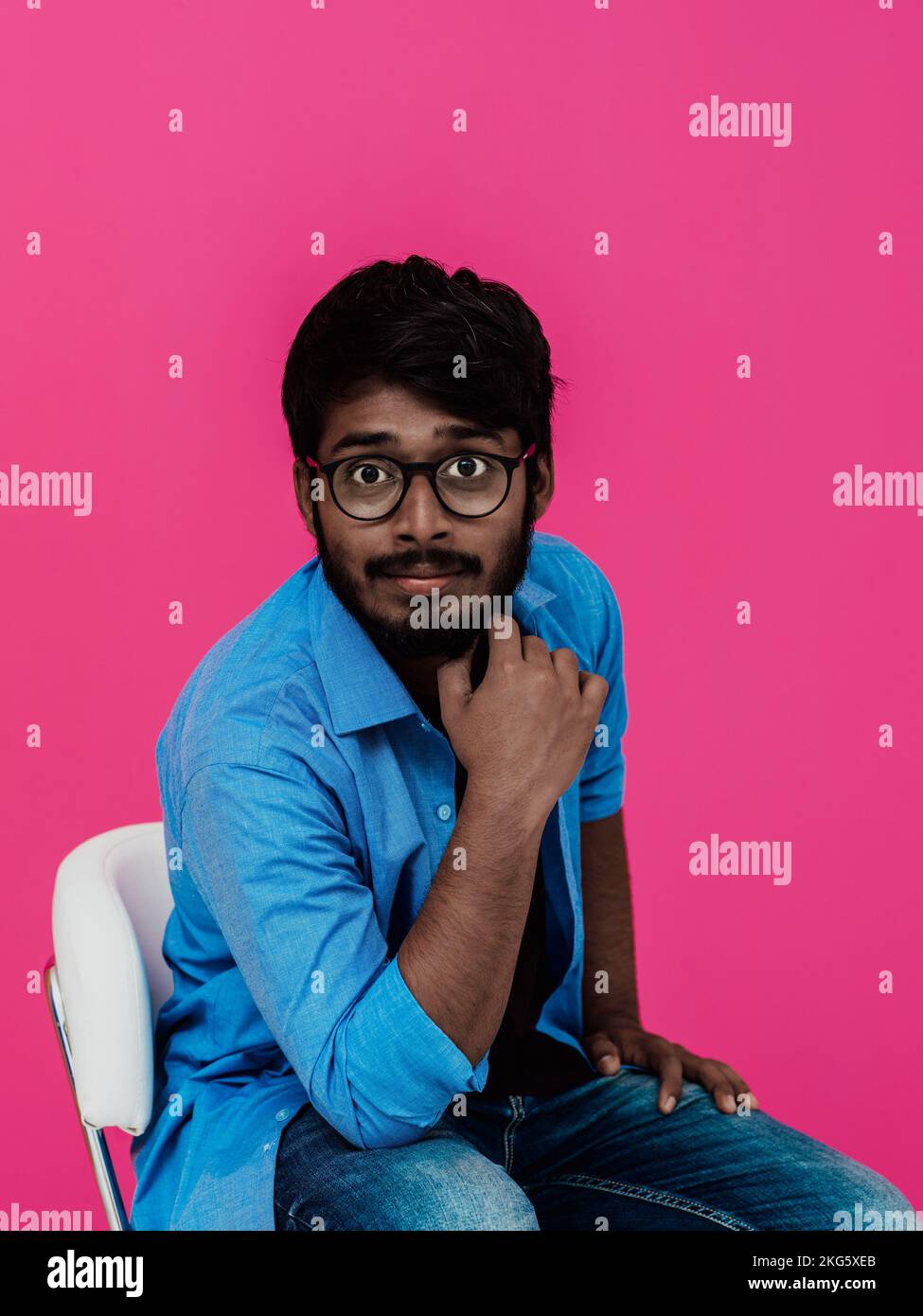 A young Indian student in a blue shirt with glasses sitting in front of ...