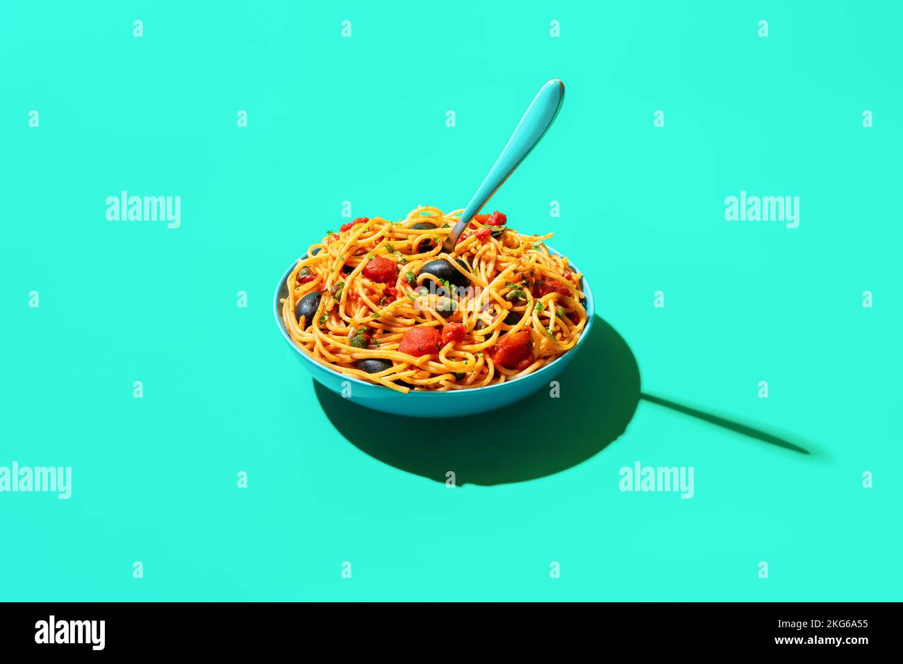 Italian dish, spaghetti with tomato sauce, black olives and capers minimalist on a green table. Vegan pasta bowl in bright light on a green background Stock Photo