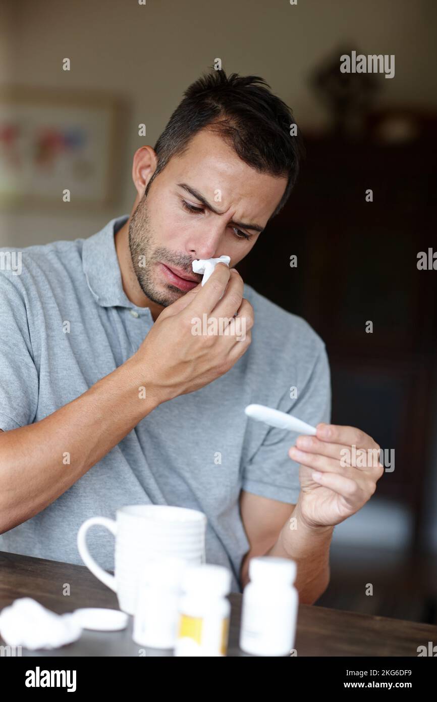 Fighting the flu. an man wiping his nose and reading his temperature on a thermometer. Stock Photo