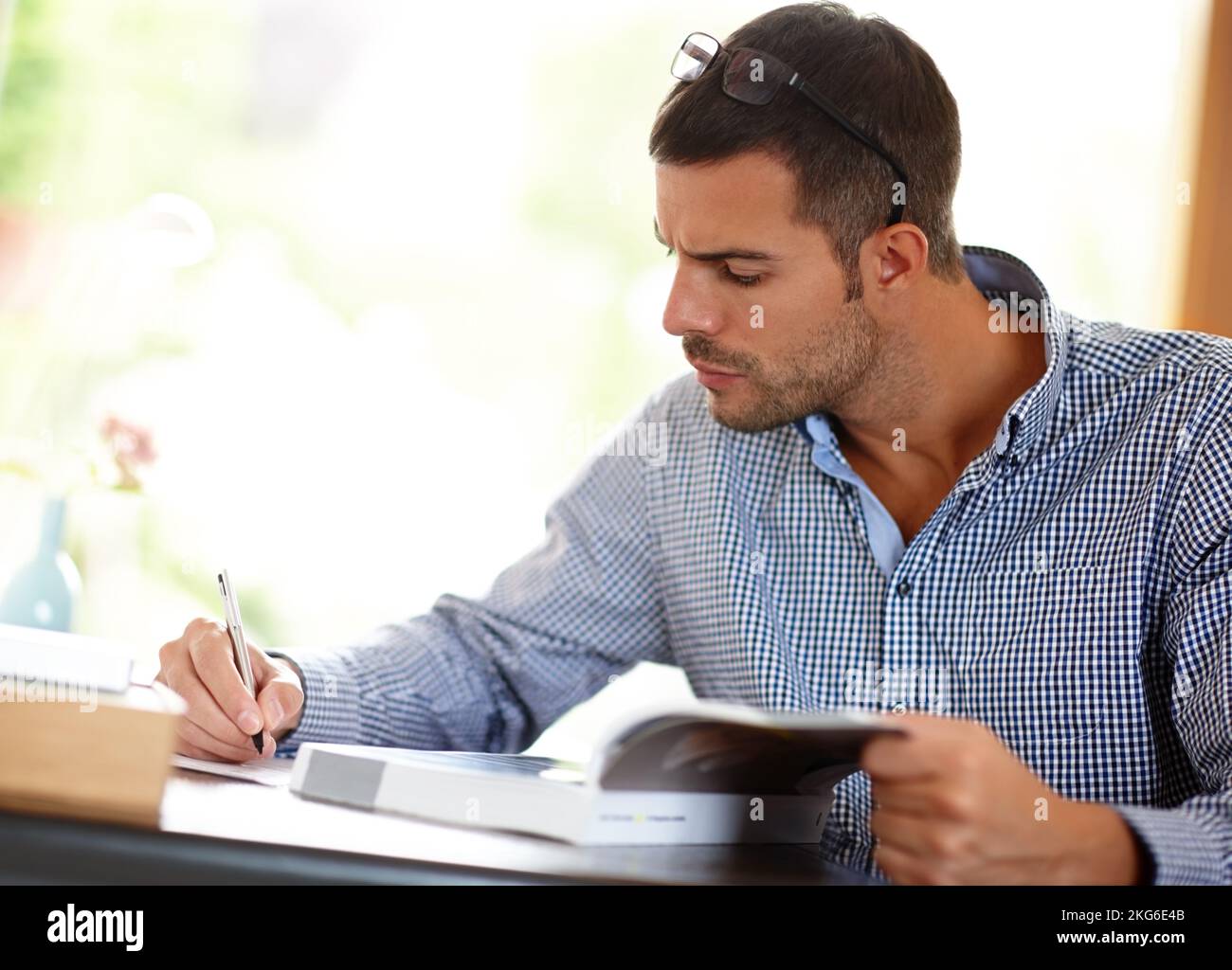 Its called continuing professional development...a young man writing notes from the book that hes studying. Stock Photo