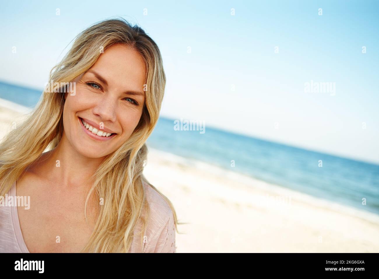 This is paradise. Head and shoulders portrait of an attractive young woman standing on a sunny beach. Stock Photo