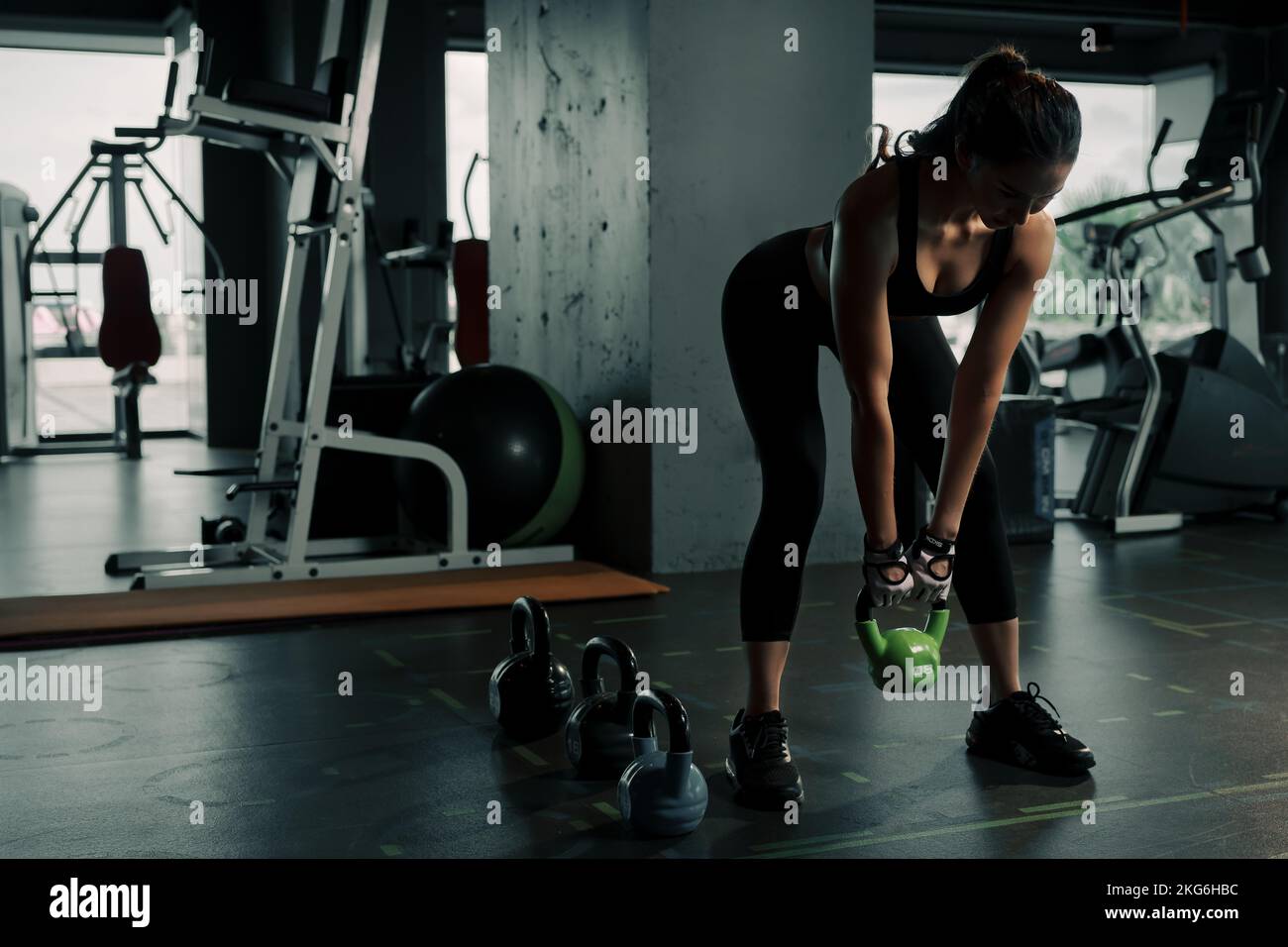 Young woman lifts single kettlebell in upper arm exercise to build muscle. Stock Photo