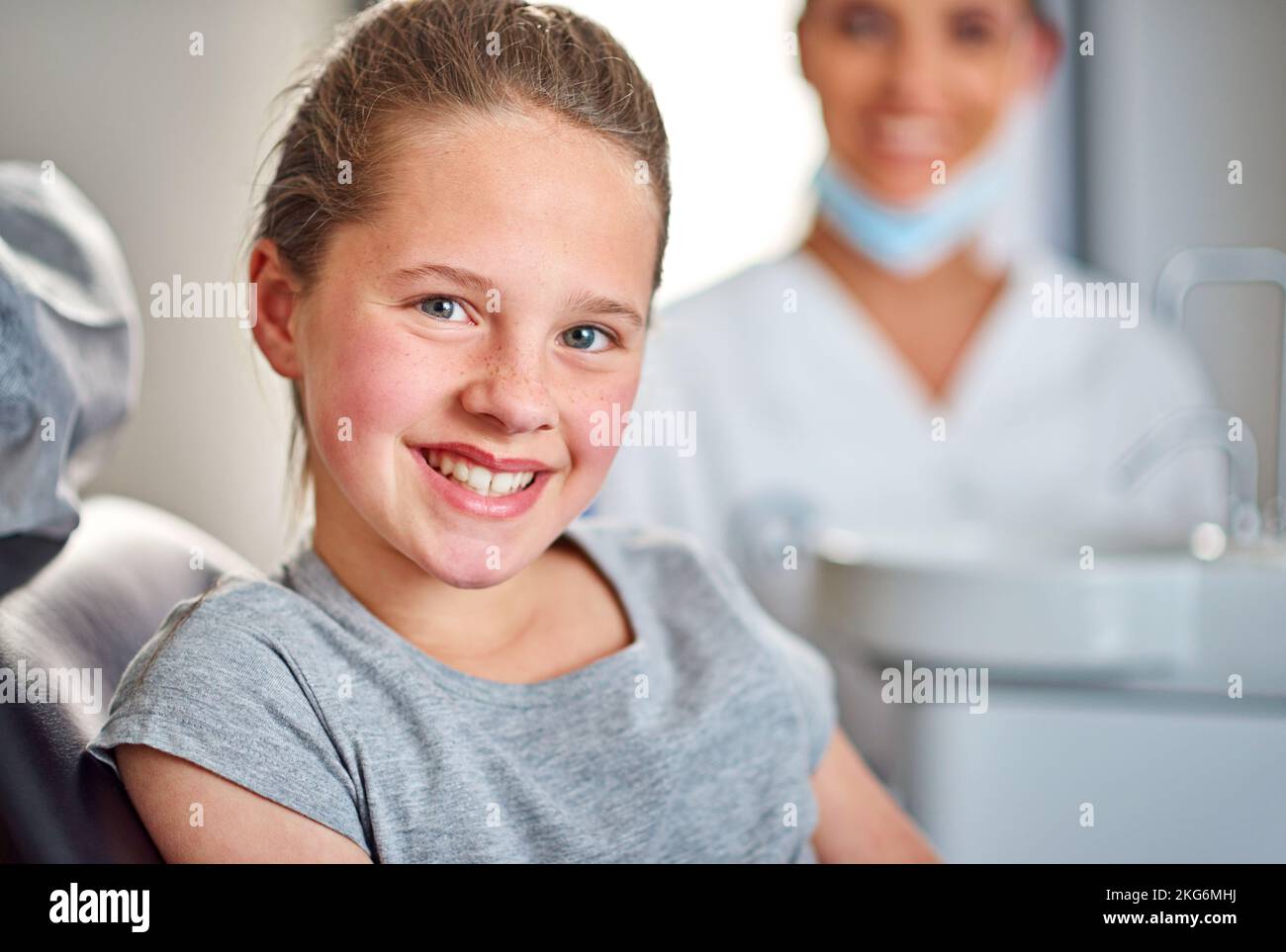 Whos afraid of the dentist Not me. A young girl sitting in a dental chair with her dentist in the background. Stock Photo
