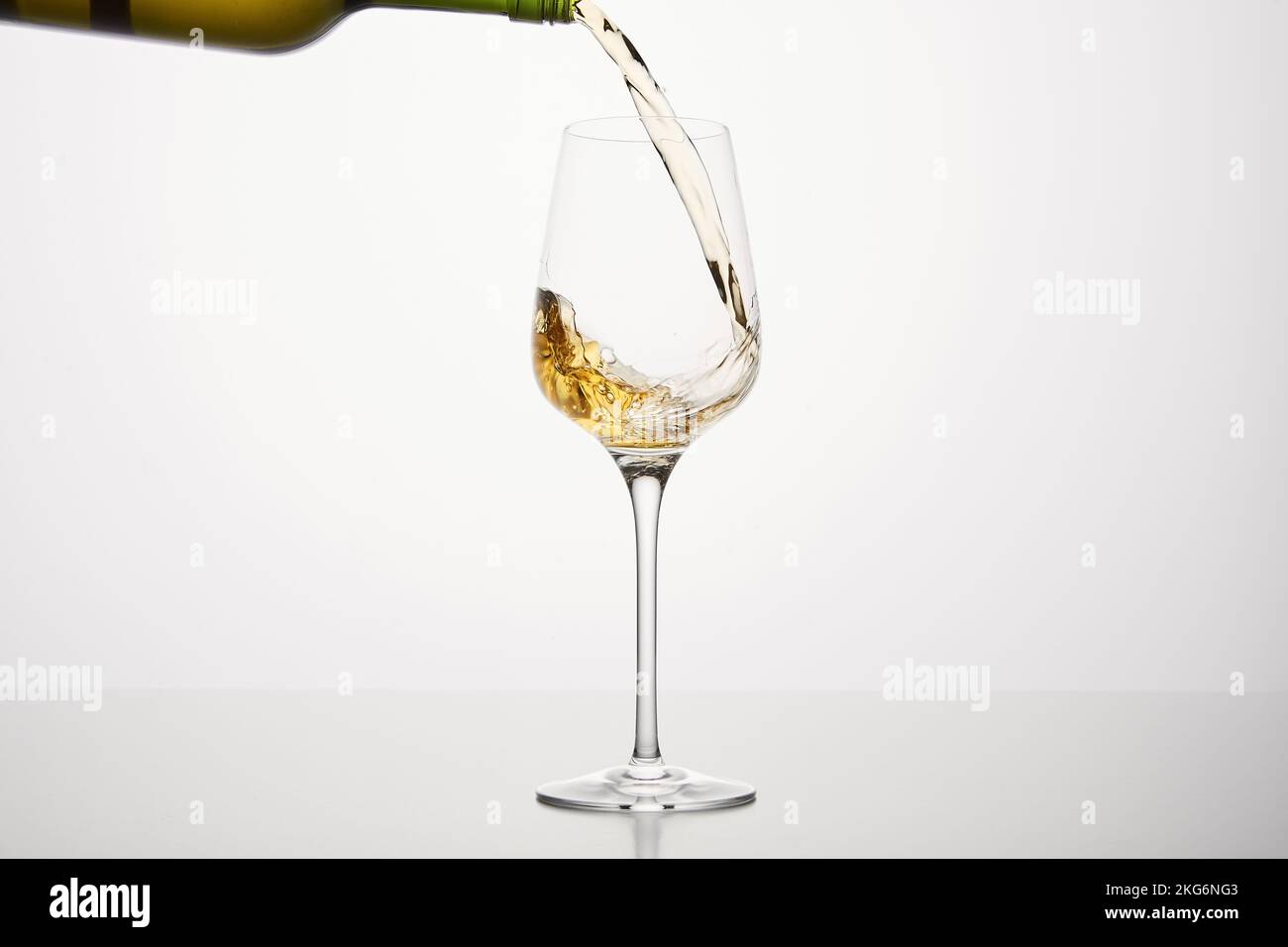 White alcohol beverage flows to wineglass, close up on white isolated. Stock Photo