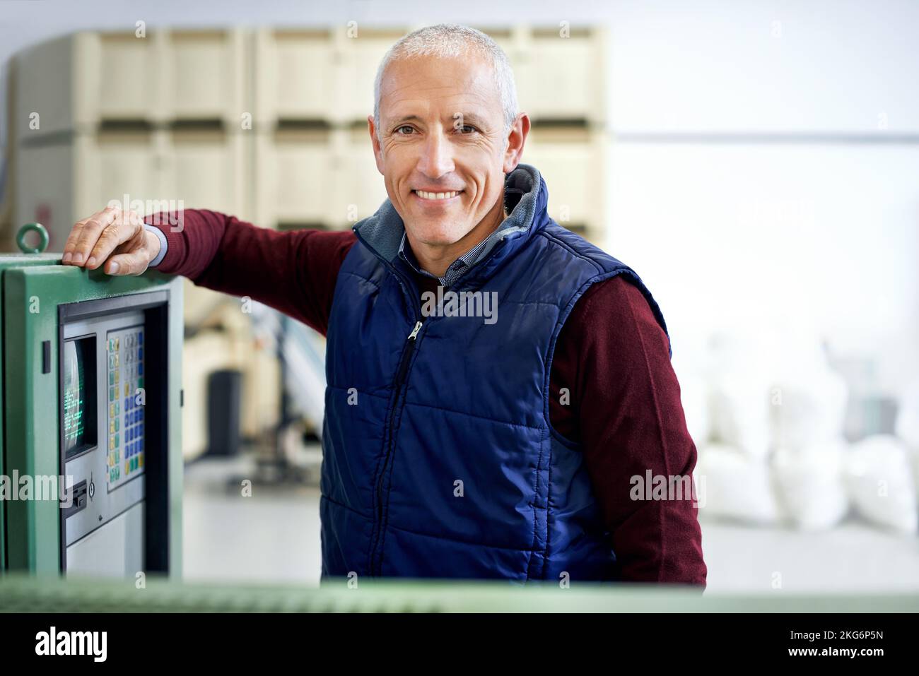 These machines run around the clock. Portrait of a mature man standing next to machinery in a factory. Stock Photo