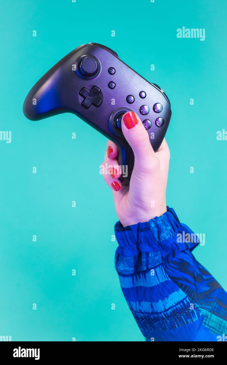 Female hand holding a video game controller gamepad isolated on a blue ...