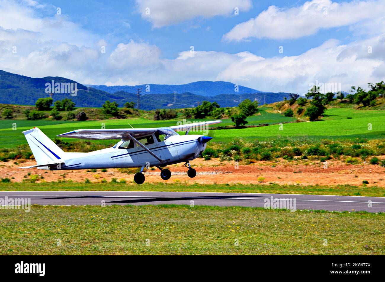 Single engine ultralight airplane taking off from airfield under blue sky with white clouds Stock Photo