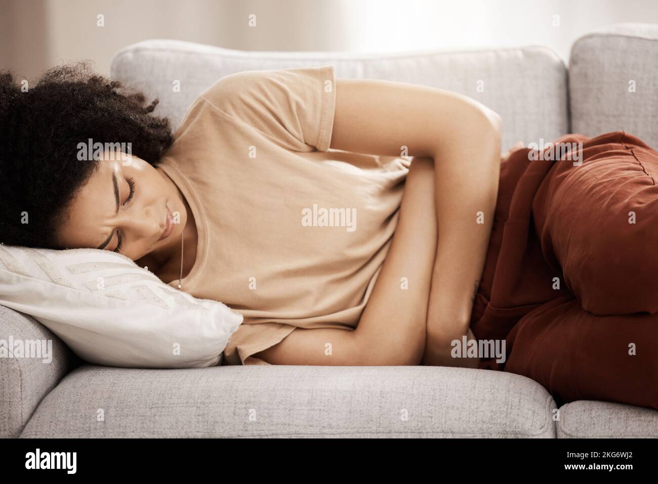 Pms, woman and stomach ache on a sofa from menstruation, period and cramps in a living room. Belly ache, black woman and pain from endometriosis Stock Photo