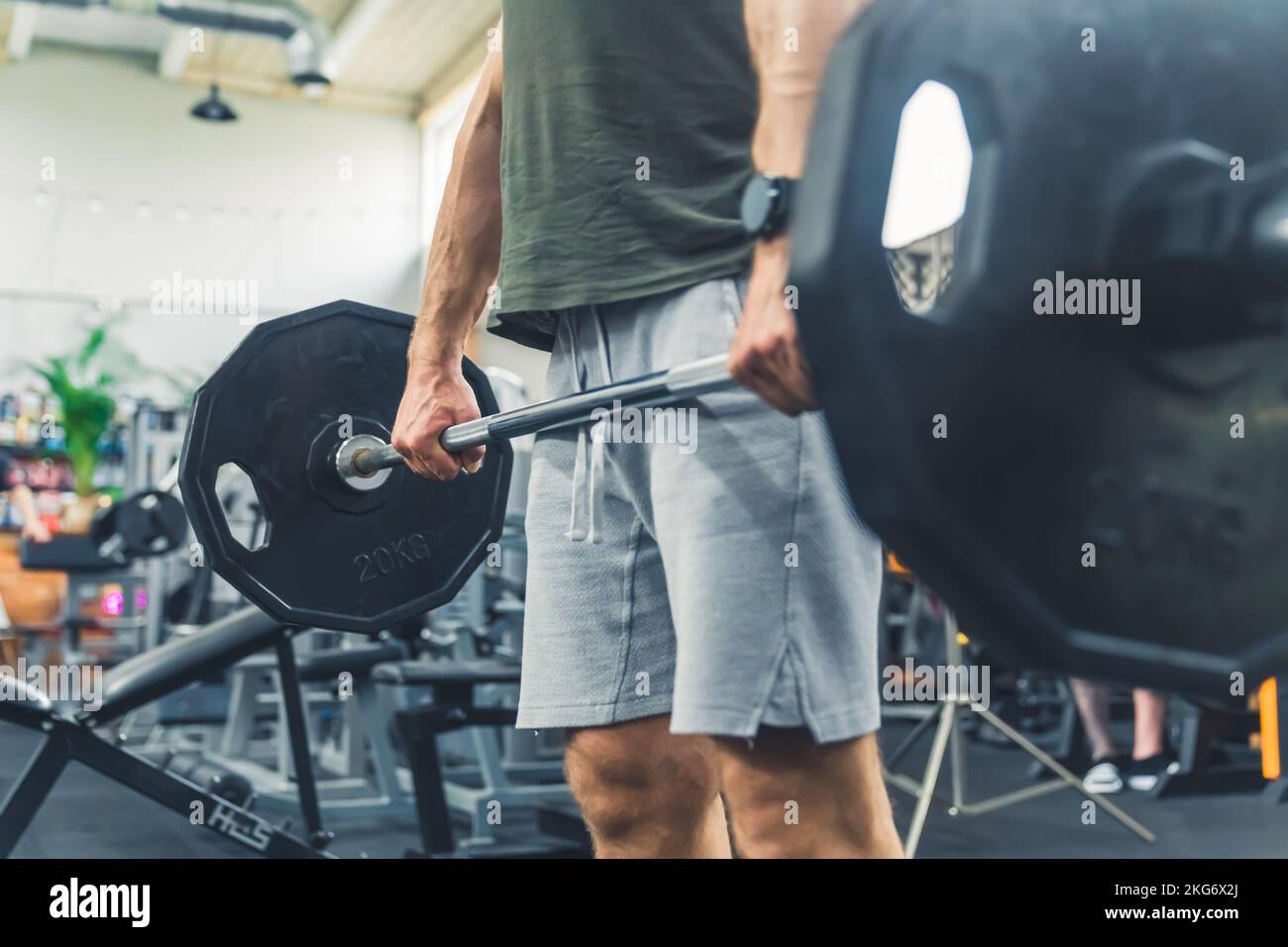 Unknown, strong, muscular man, bodybuilder, in grey shorts and a t-shirt, standing straight, holding a barbell loaded with heavy plates. High quality photo Stock Photo