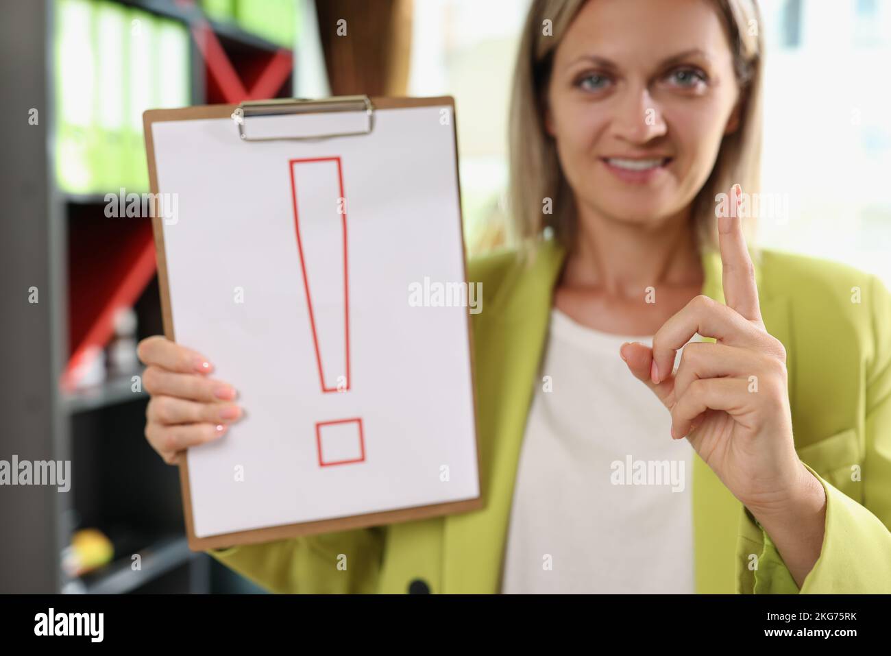 Smiling woman holding clipboard with red exclamation point Stock Photo