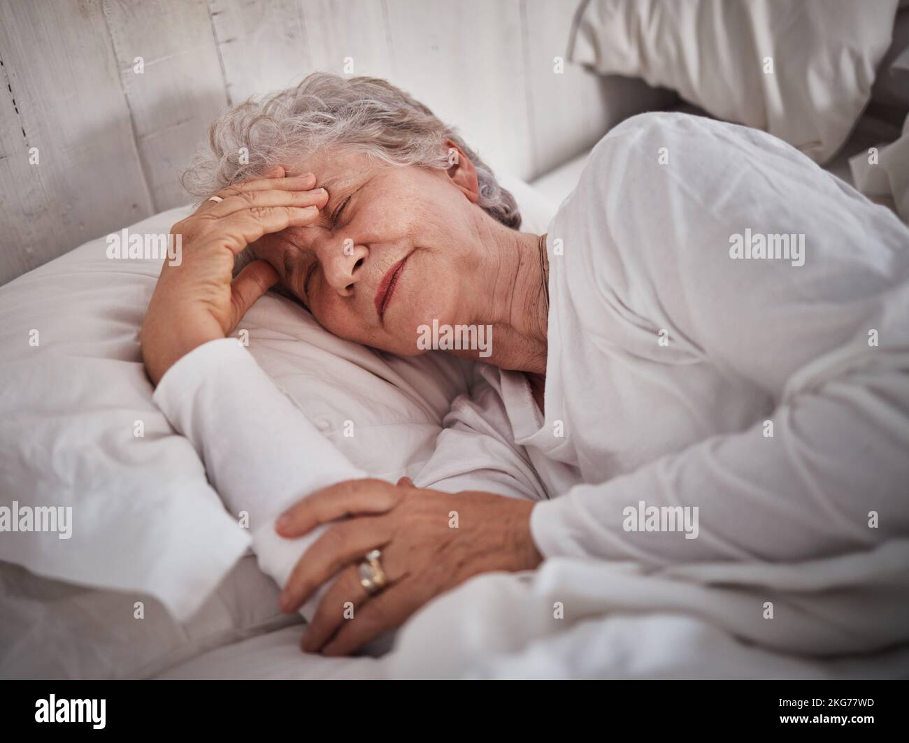 Elderly woman, sleeping and bed with headache to rest mind, tired body and dreaming for wellness in house. Senior lady, home bedroom and pain while Stock Photo