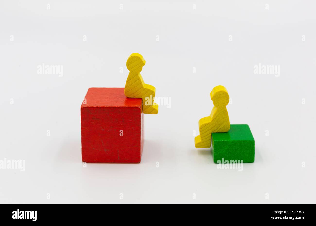 two wooden figures of people sitting on top of high and low boxes..social relationships, male-female relationship, differences and figures. Banner Stock Photo