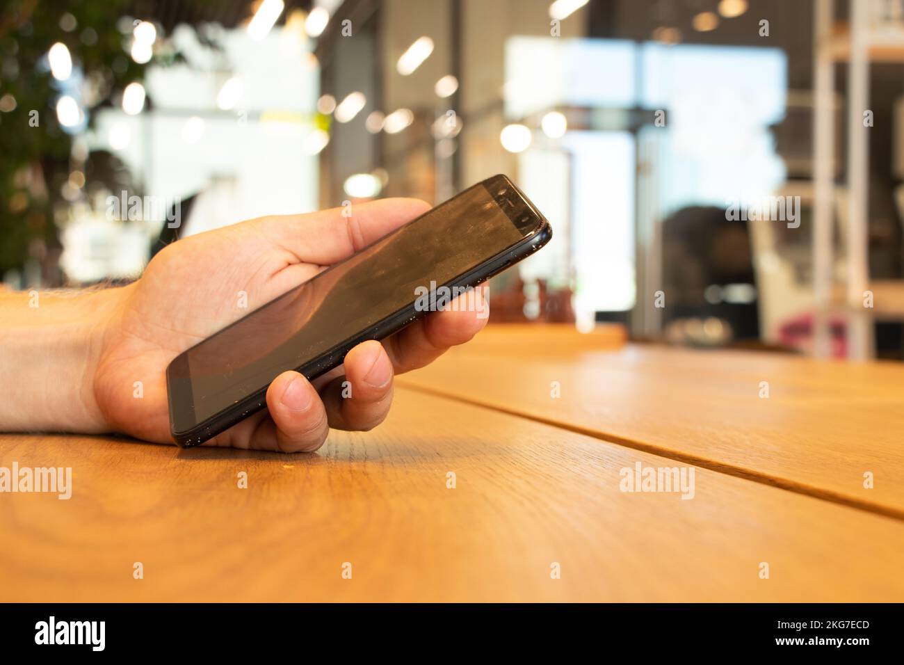 a mobile phone in the hand of a man at a table in a cafe, a phone in his hands Stock Photo