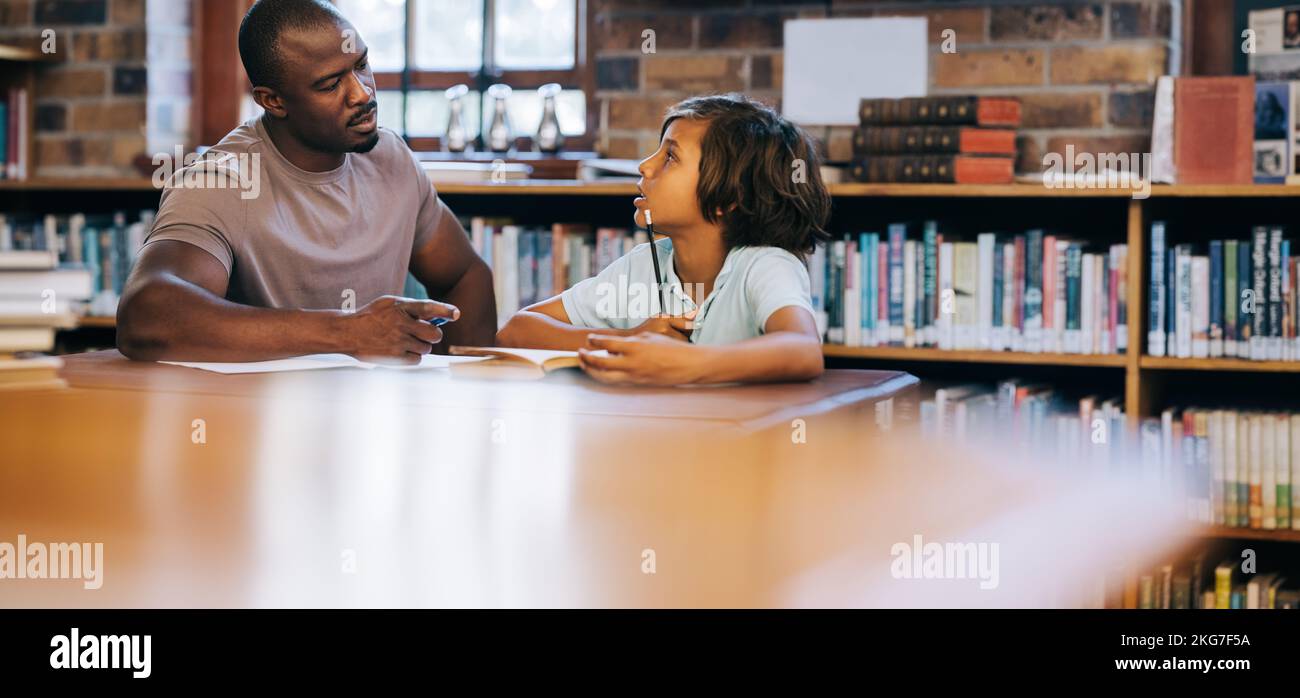Teacher counselling a young student in a school library. Primary school teacher talking to a school boy in a private session. Child therapy and suppor Stock Photo