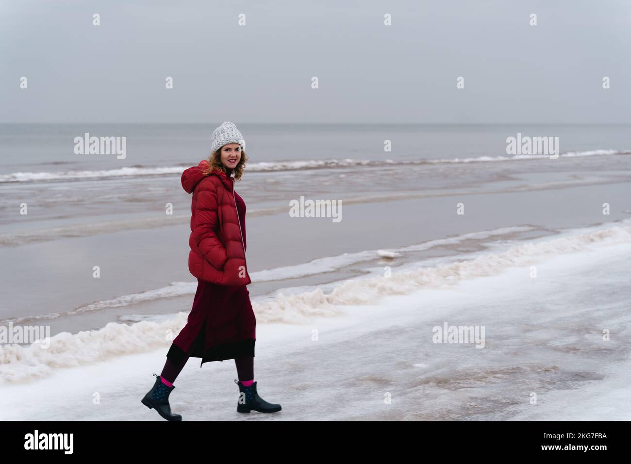 A woman in red warm clothes walks along the sea in winter. Stock Photo