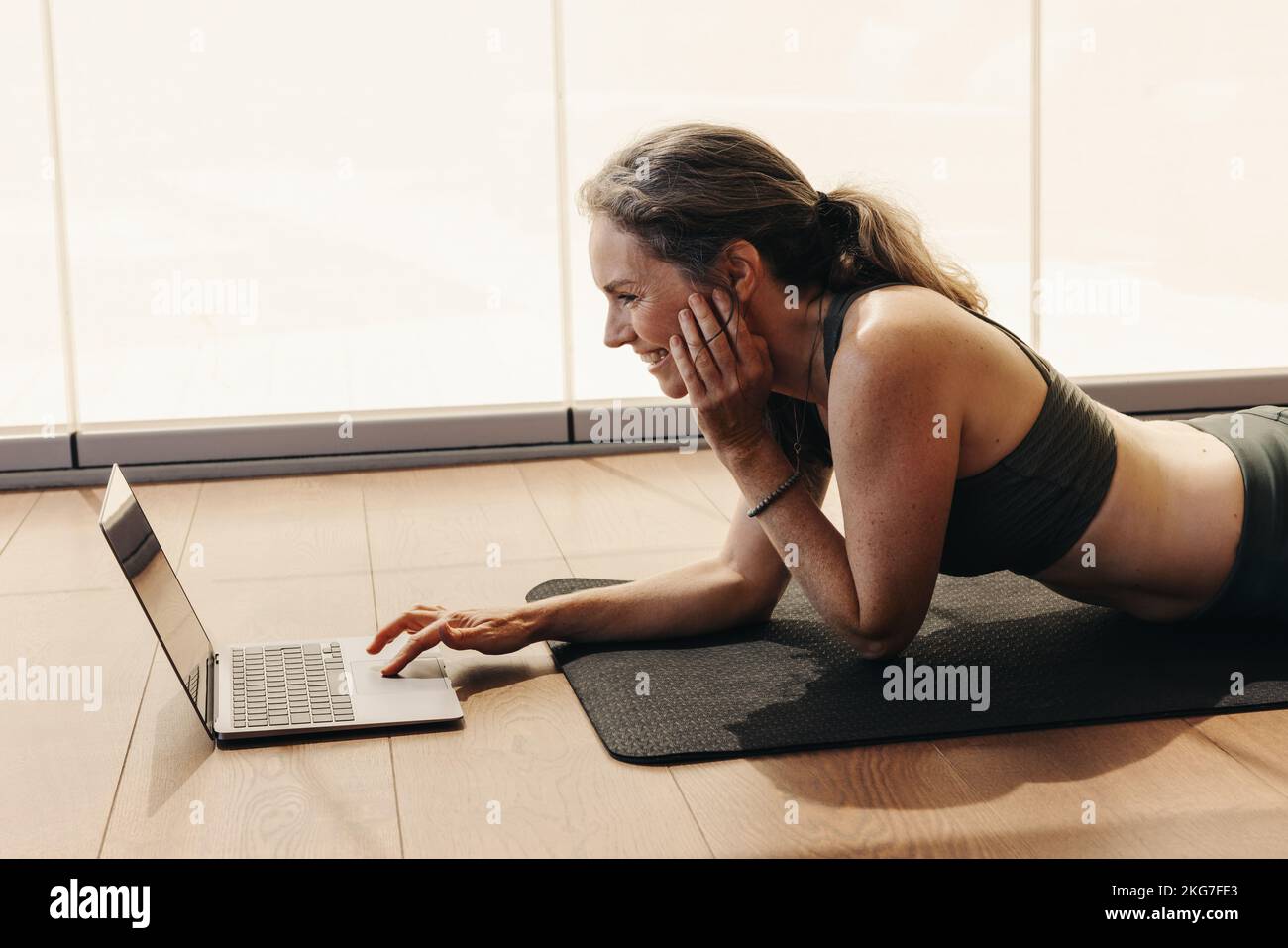 Cheerful senior woman smiling while joining a virtual yoga class on a laptop. Woman following an online workout tutorial at home. Happy mature woman l Stock Photo