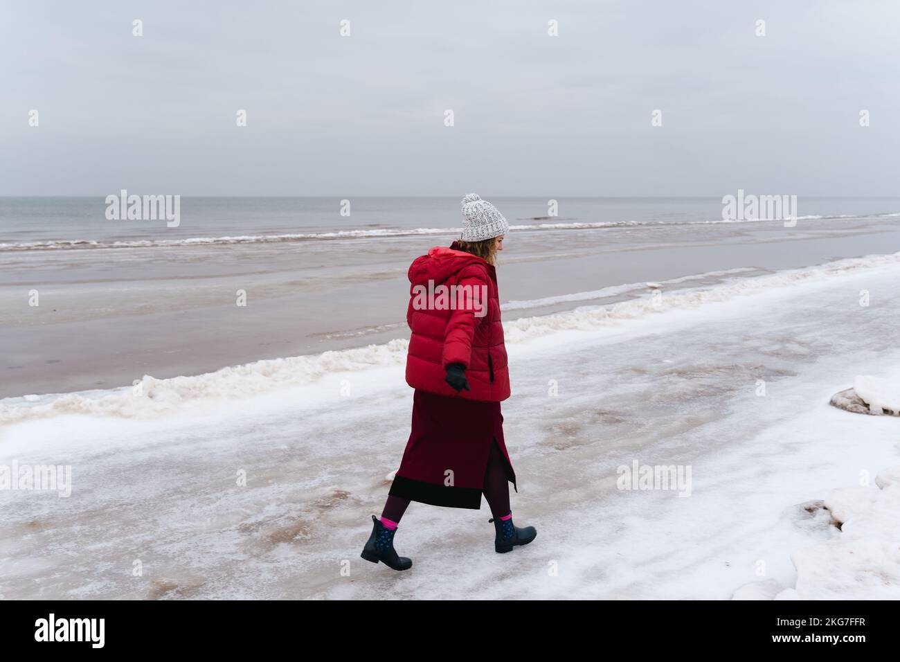 A woman in warm clothes walks along the sea in winter. Stock Photo