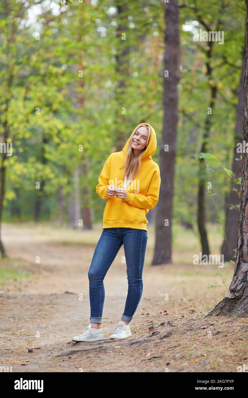 Beautiful young blonde woman in yellow hoodie walks in the park ...