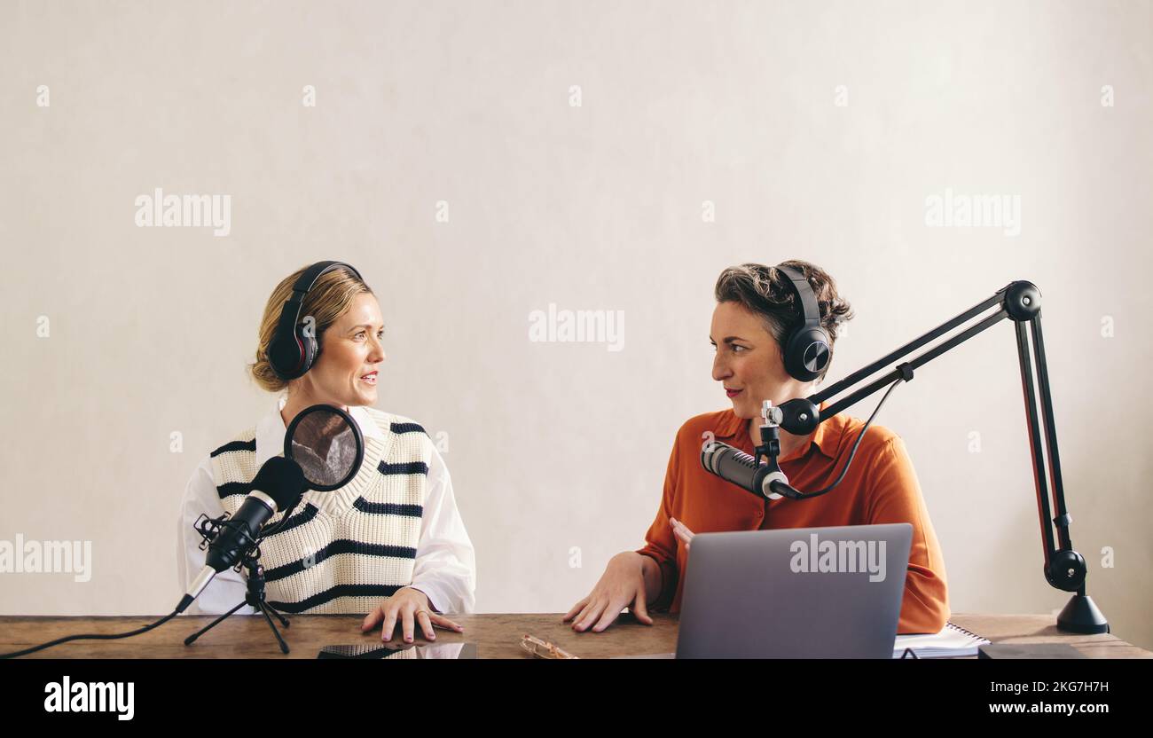 Two female podcasters having a conversation while co-hosting an a show in a home studio. Two women recording an audio broadcast for their social media Stock Photo