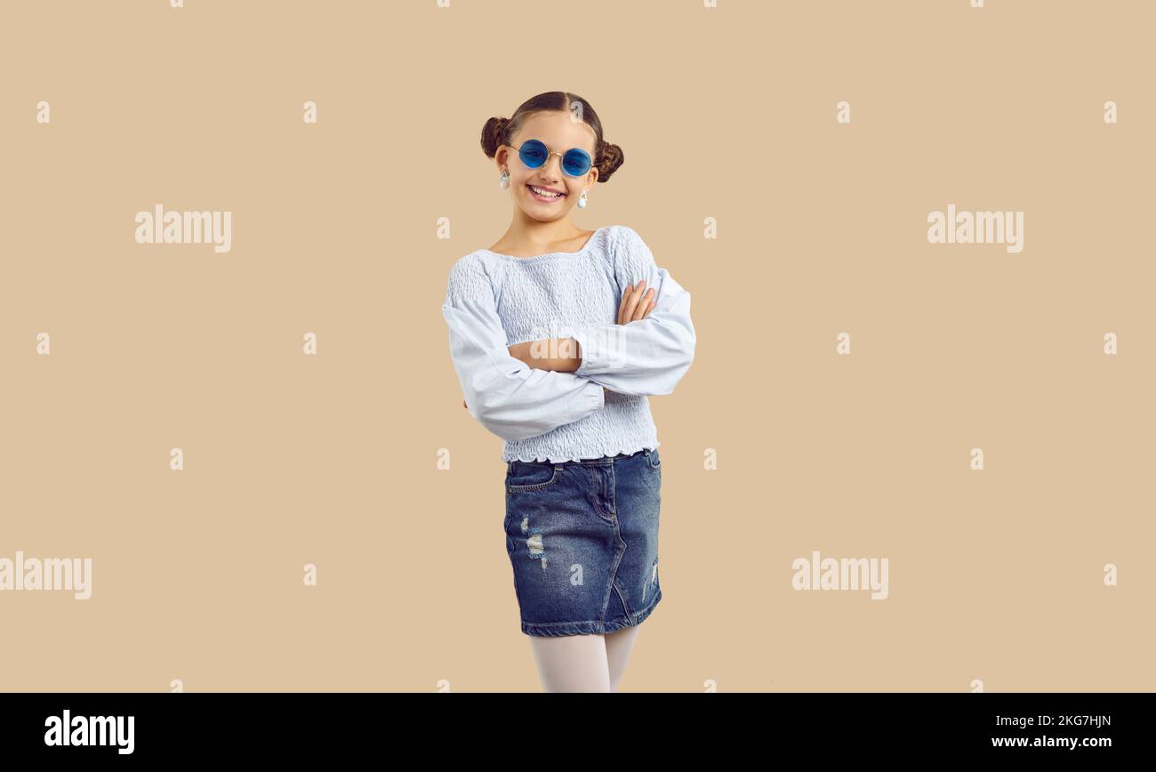 Happy pretty girl in trendy casual outfit and sunglasses posing on beige background Stock Photo