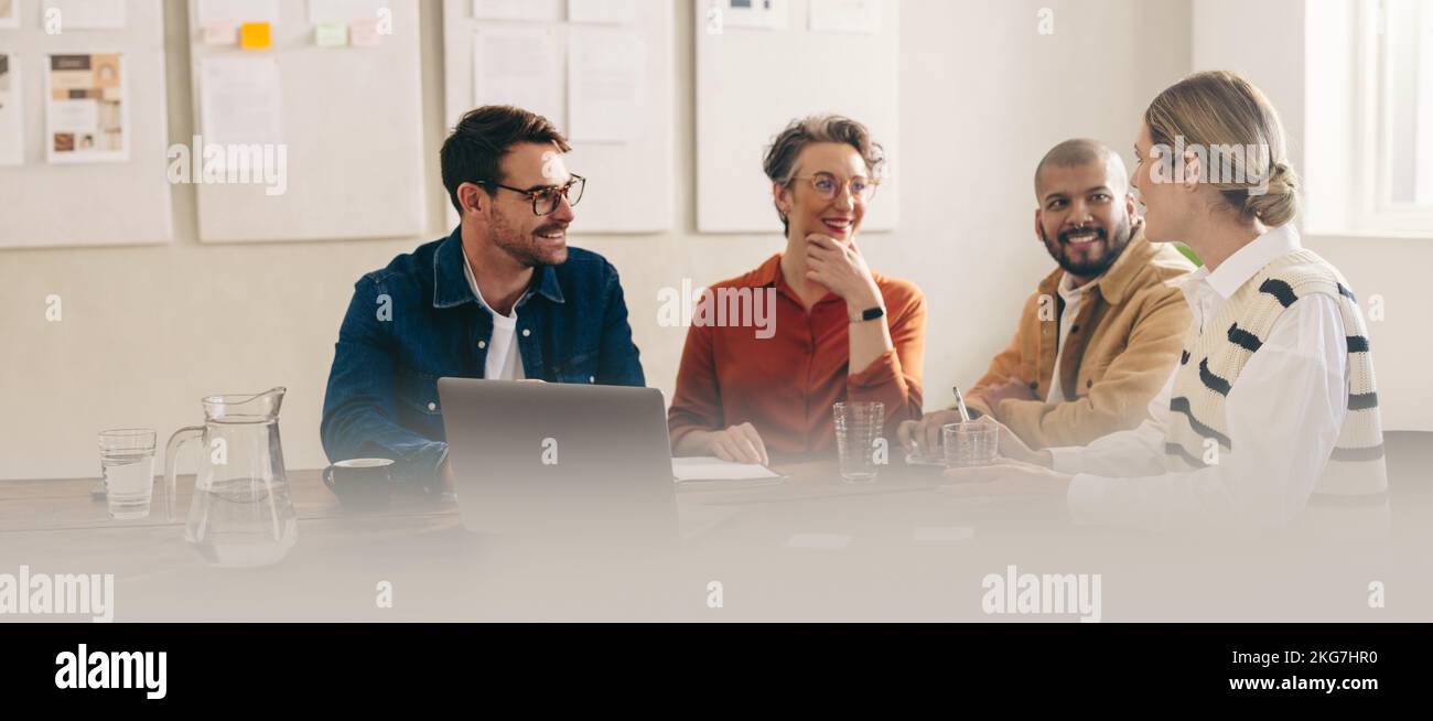 Happy businesspeople smiling while having a meeting in a creative office. Group of cheerful business colleagues sharing ideas while working together o Stock Photo