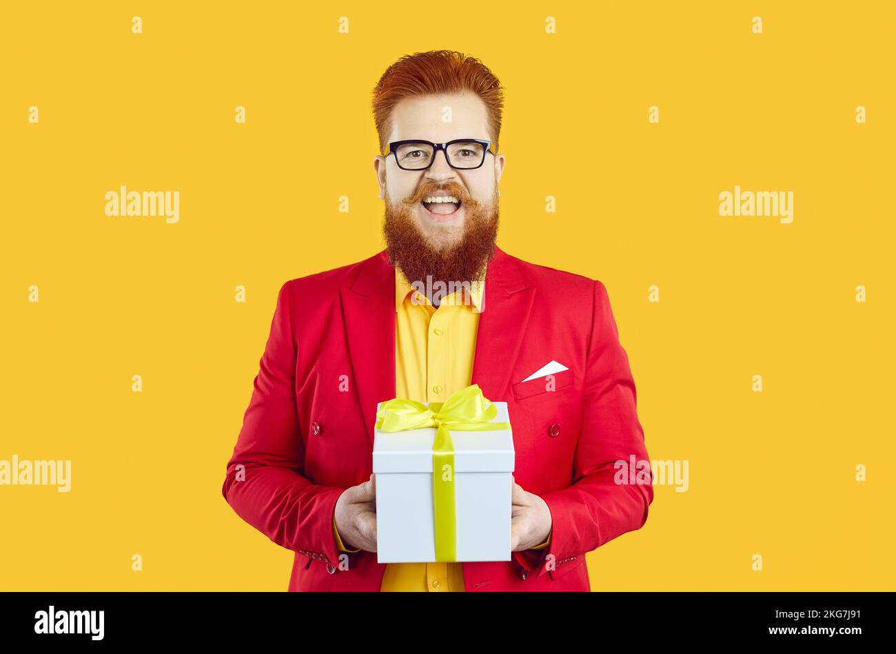 Extravagant stylish chubby man presents you with gift standing on orange background. Stock Photo