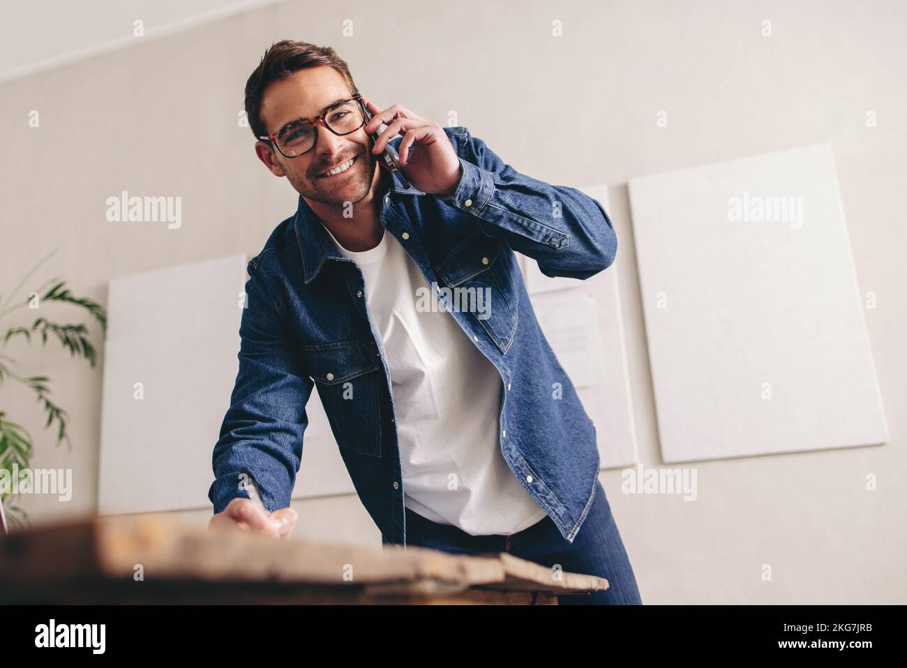 Happy businessman smiling and writing notes during a phone call. Cheerful businessman making plans with his clients over the phone. Businessman with g Stock Photo