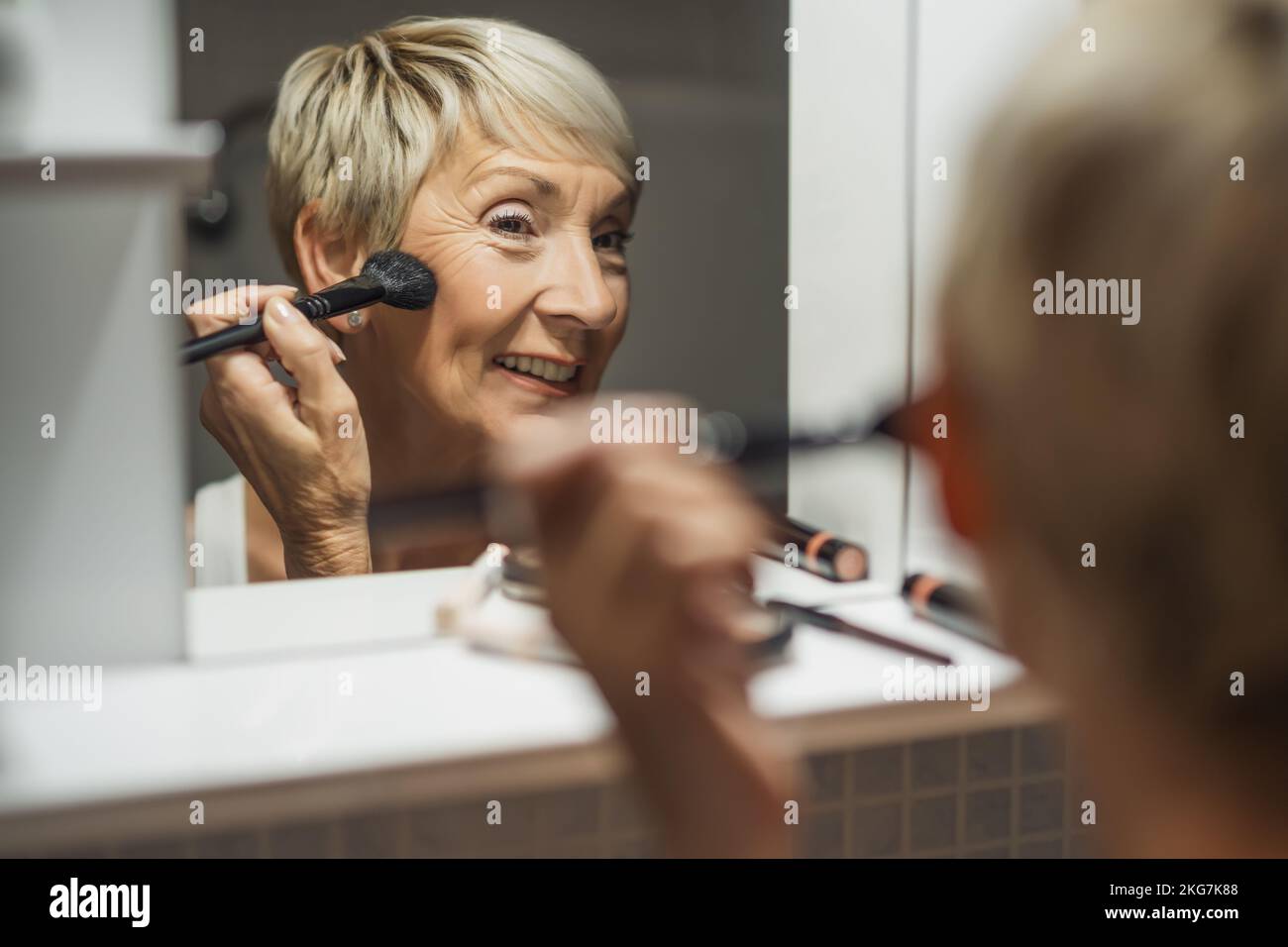 Mature woman is applying blush in the bathroom. Stock Photo