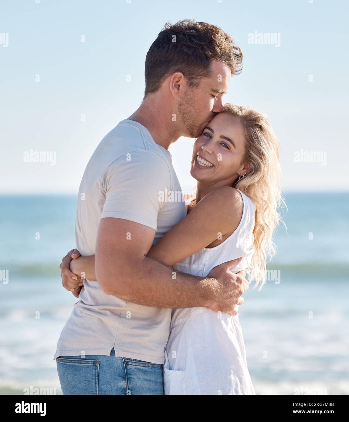 Couple, beach and hug bonding with a kiss, love and care happy about anniversary and commitment. Portrait of a girlfriend and boyfriend together on Stock Photo