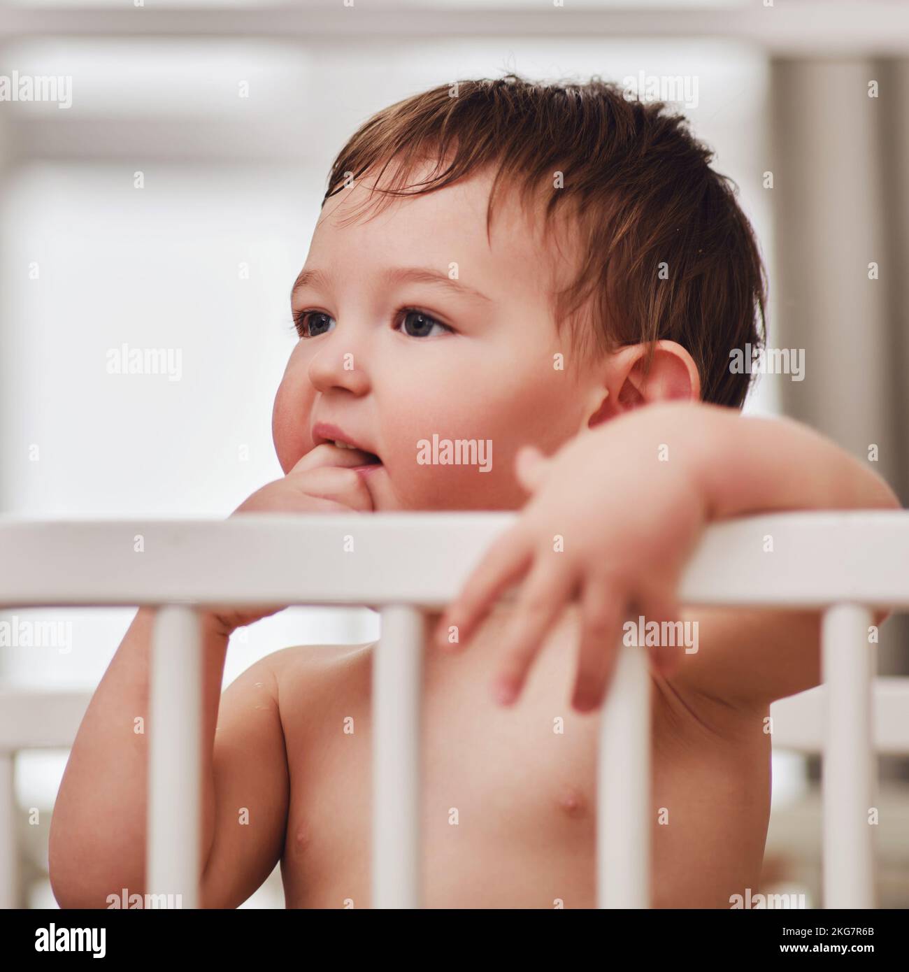 Toddler baby stands thinking in the crib, closeup portrait. The child