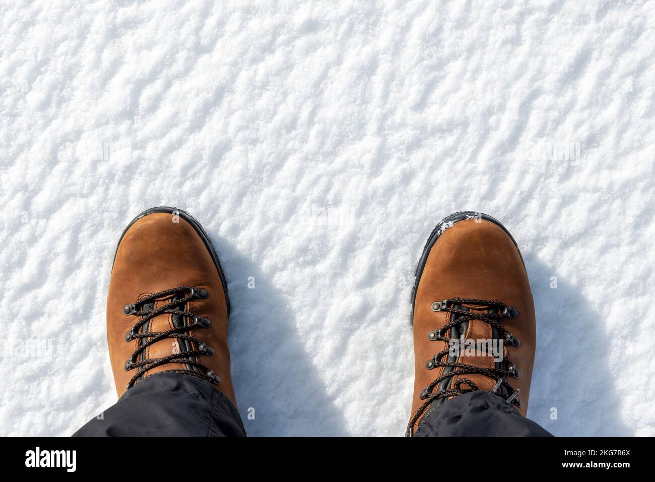 Closeup top above view of male foots in brown leather warm boots isolated on white icy snow surface background. Detail waterproof shoes. Winter Stock Photo