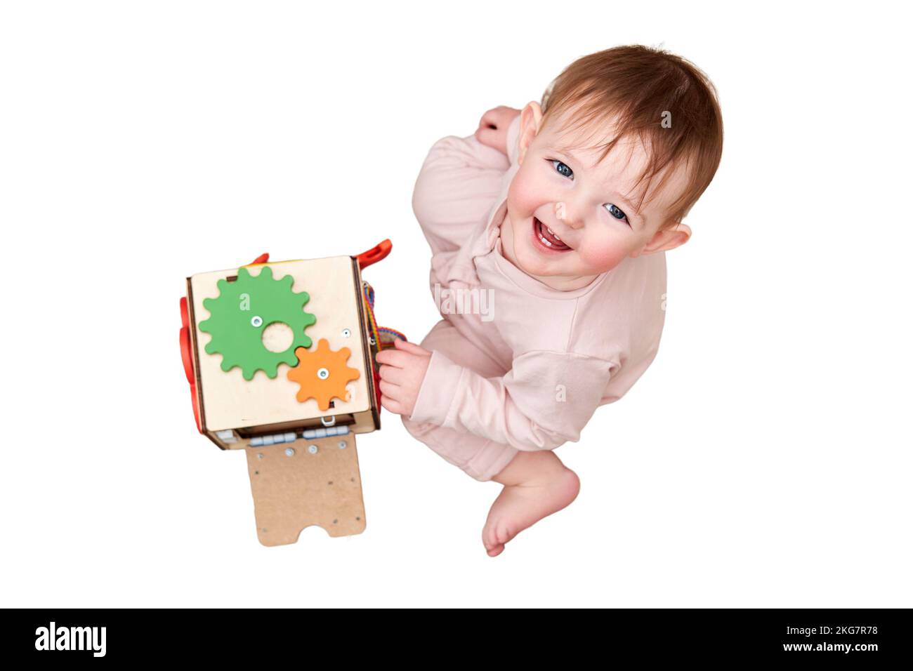 Happy toddler baby boy is playing with a busyboard cube on the nursery floor, isolated on a white background. Educational toys for children, wooden ga Stock Photo