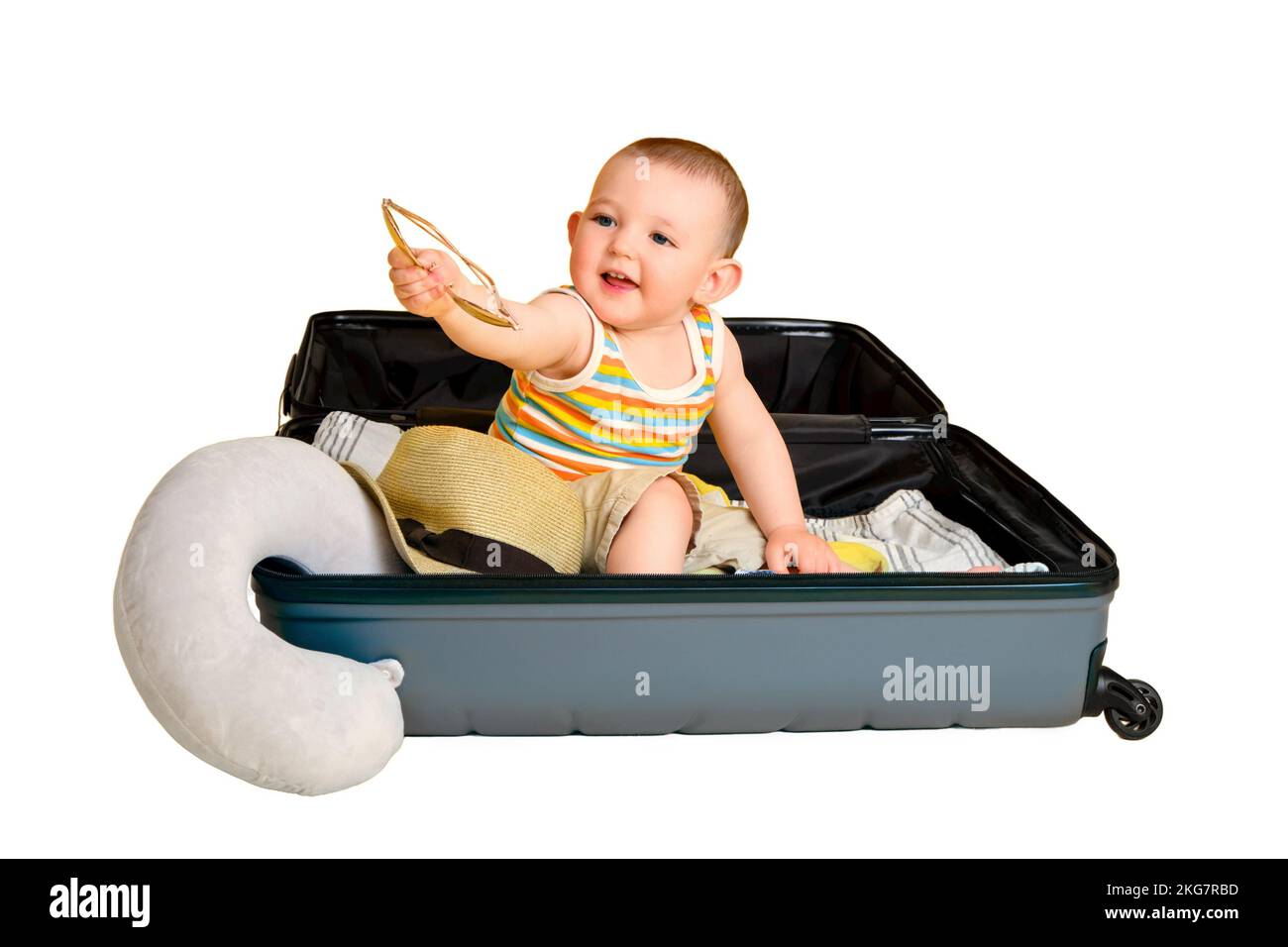 Baby toddler boy sits inside a suitcase with clothes, studio isolated on white background. A