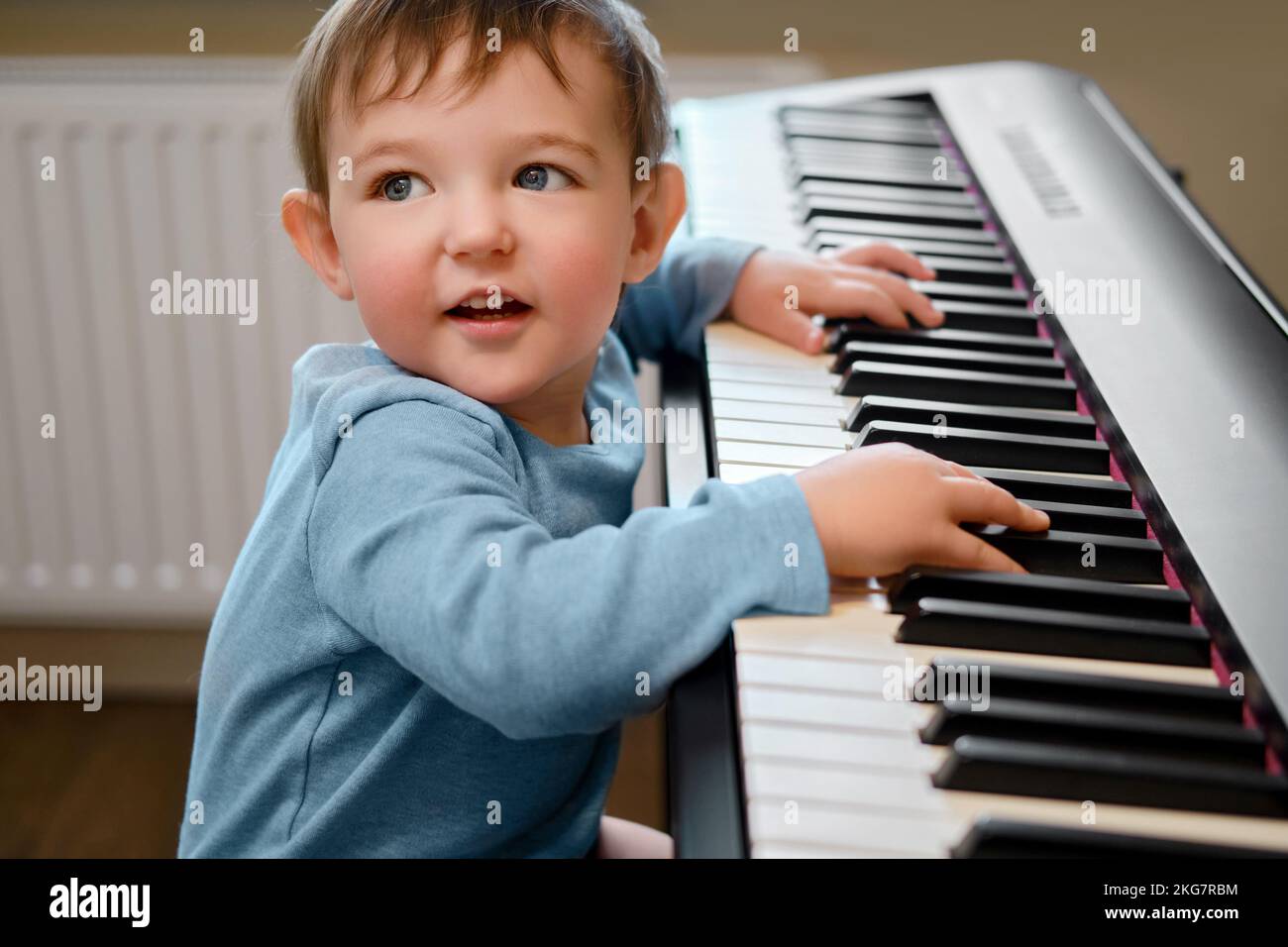 Toddler baby plays piano in home living room, music lessons. Happy