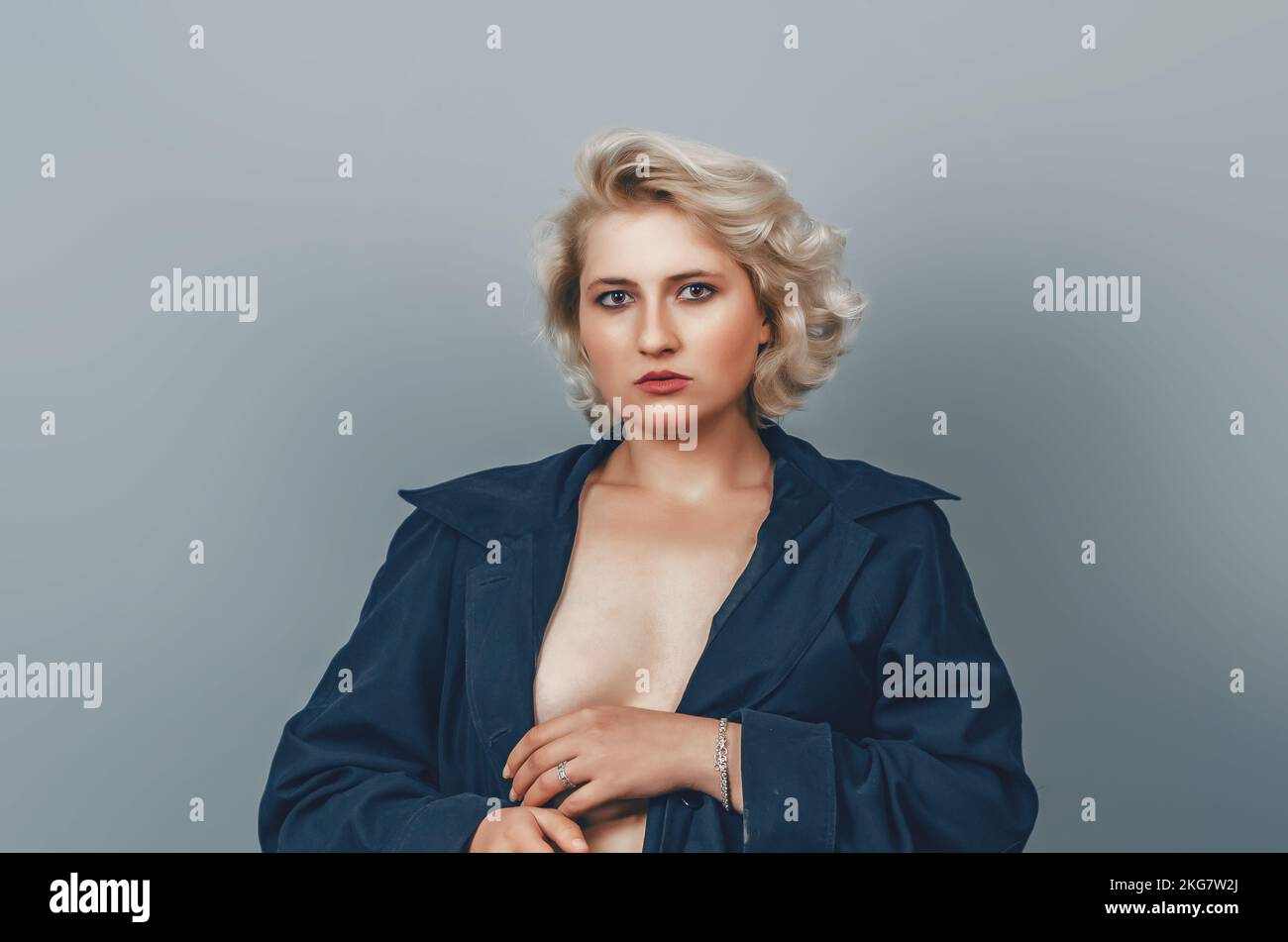 Pretty topless blonde girl in black raincoat, hand near face, looking at camera. Stock Photo
