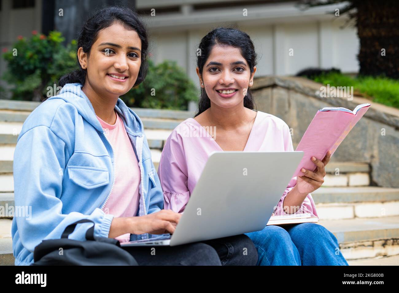 focus on girl with book, Happy College students looking at camera while busy working on laptop on university campus - concept of education, teamwork Stock Photo